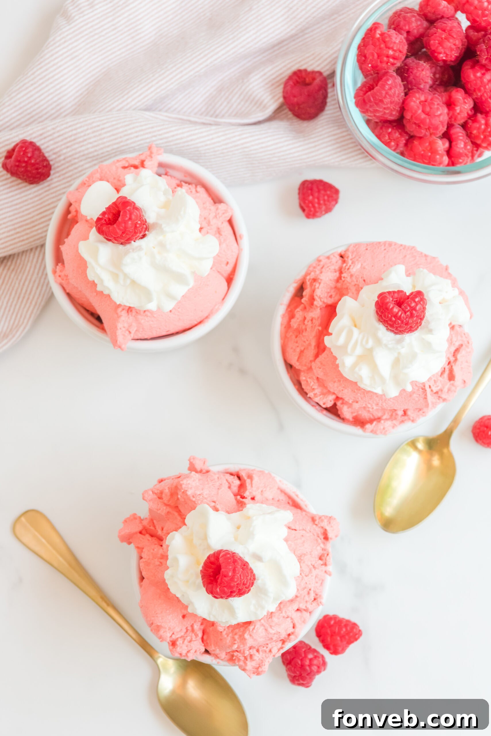 Luscious Raspberry Whip 6 Overhead view of Raspberry Jello Fluff in three white dishes garnished with whipped cream and fresh raspberries, highlighting the festive presentation.
