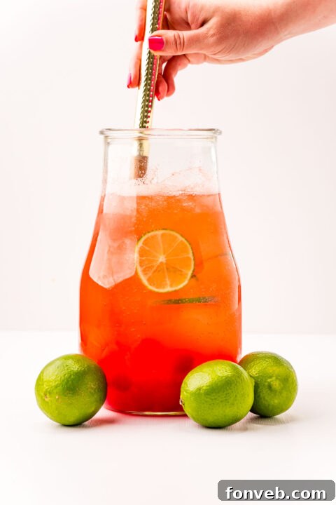 Crimson Zest Quencher 11 A freshly poured glass of Cherry Limeade, garnished with a lime and cherry, sitting alongside the pitcher, emphasizing the final product.