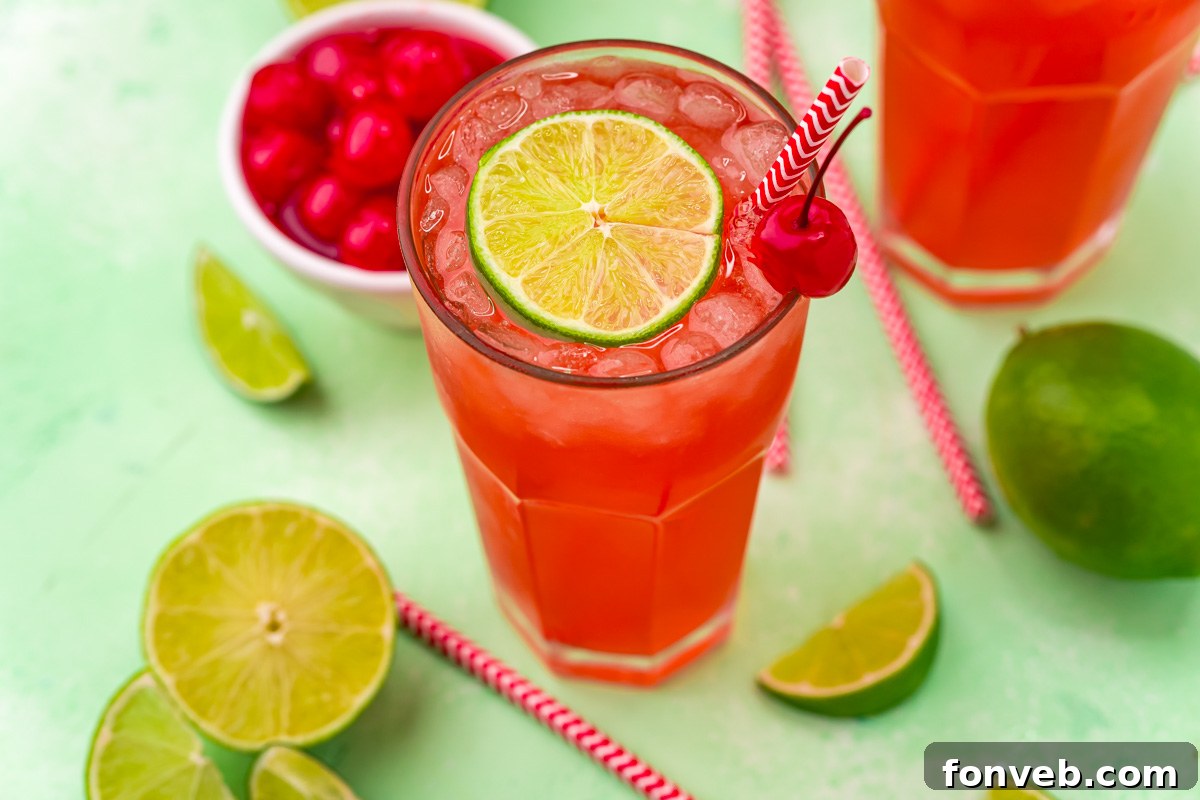 Crimson Zest Quencher 12 A 45-degree angle view of a glass of refreshing Cherry Limeade, garnished with a lime wedge and a maraschino cherry, set against a bright, summery background.