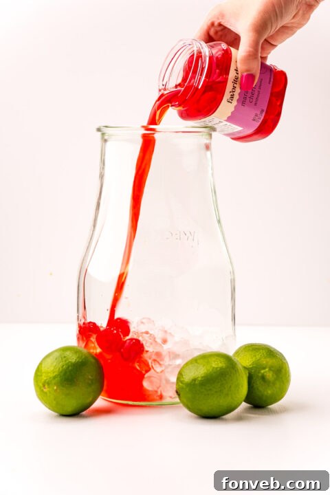 Crimson Zest Quencher 6 Close-up of a hand pouring vibrant red cherry syrup into a glass pitcher as part of the Cherry Limeade preparation process.