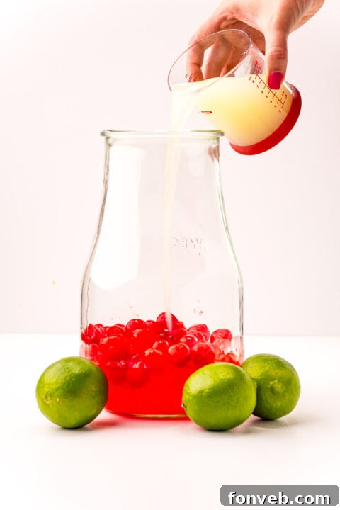 Crimson Zest Quencher 7 A pitcher being filled with the various liquid ingredients for Cherry Limeade, showcasing the layering of colors before mixing.