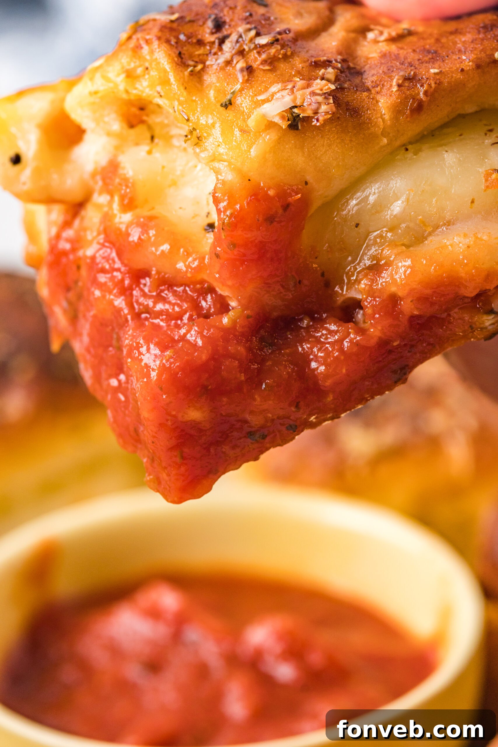 Ultimate Pizza Pull-Aparts 16 A close-up view of a single pizza slider being dipped into a bowl of marinara sauce, showing the melted cheese and pepperoni.