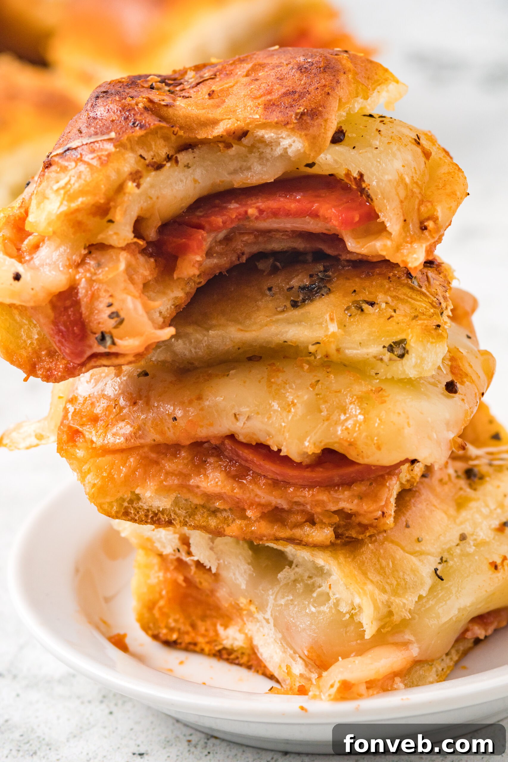 Ultimate Pizza Pull-Aparts 3 Three pizza sliders stacked on top of each other on a white plate with a bite removed from the top slider, showcasing gooey cheese and pepperoni.