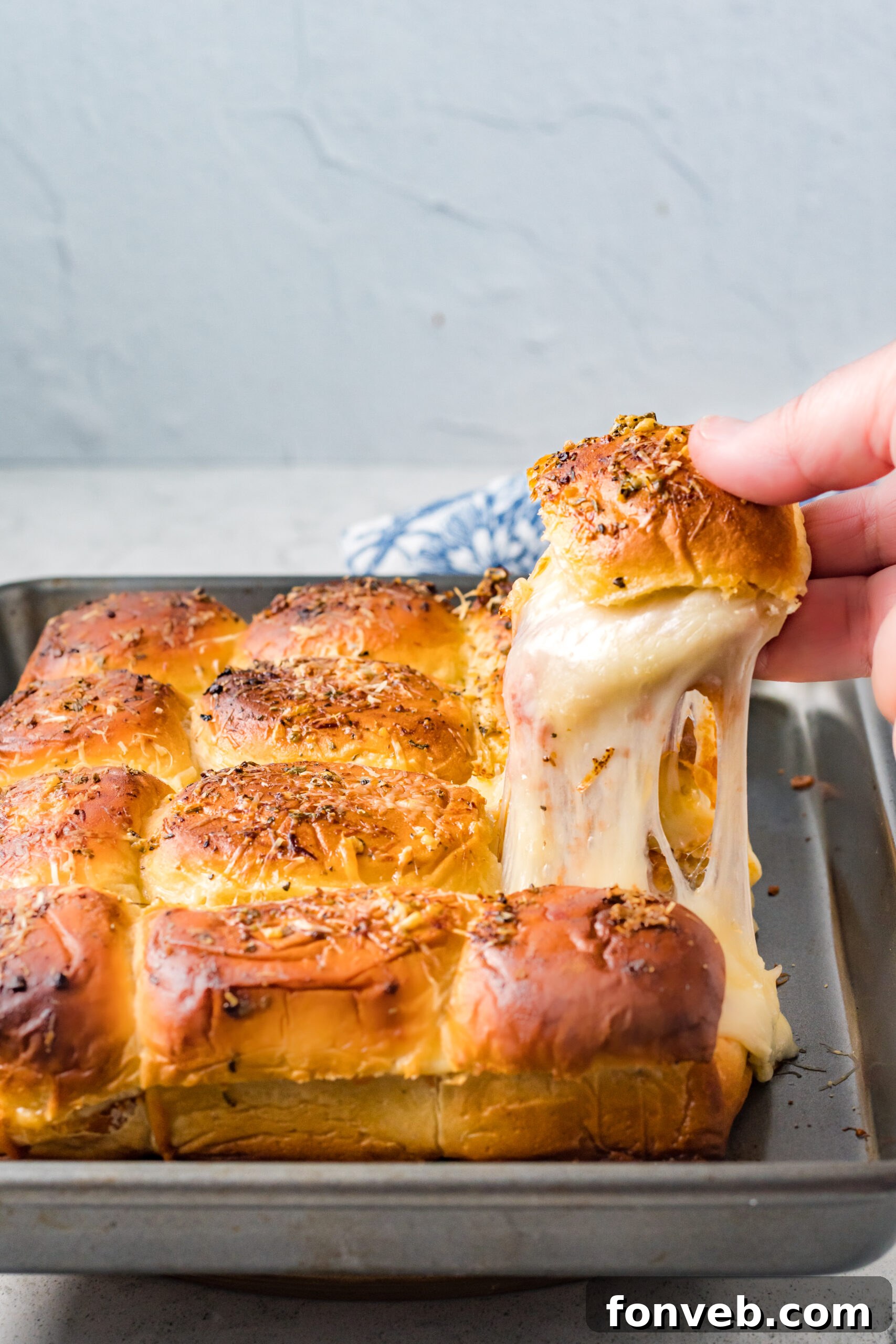 Ultimate Pizza Pull-Aparts 6 A pizza slider being carefully lifted from a baking tray, showcasing an impressive cheese pull.
