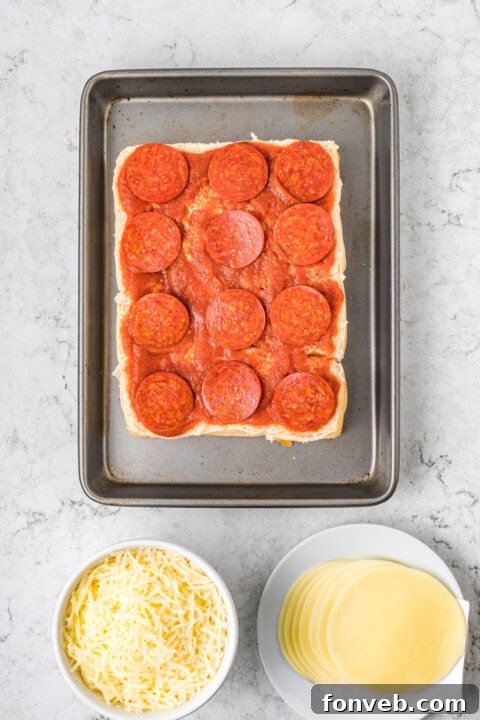 Ultimate Pizza Pull-Aparts 10 Pizza sauce being spread evenly over the bottom layer of Hawaiian rolls.