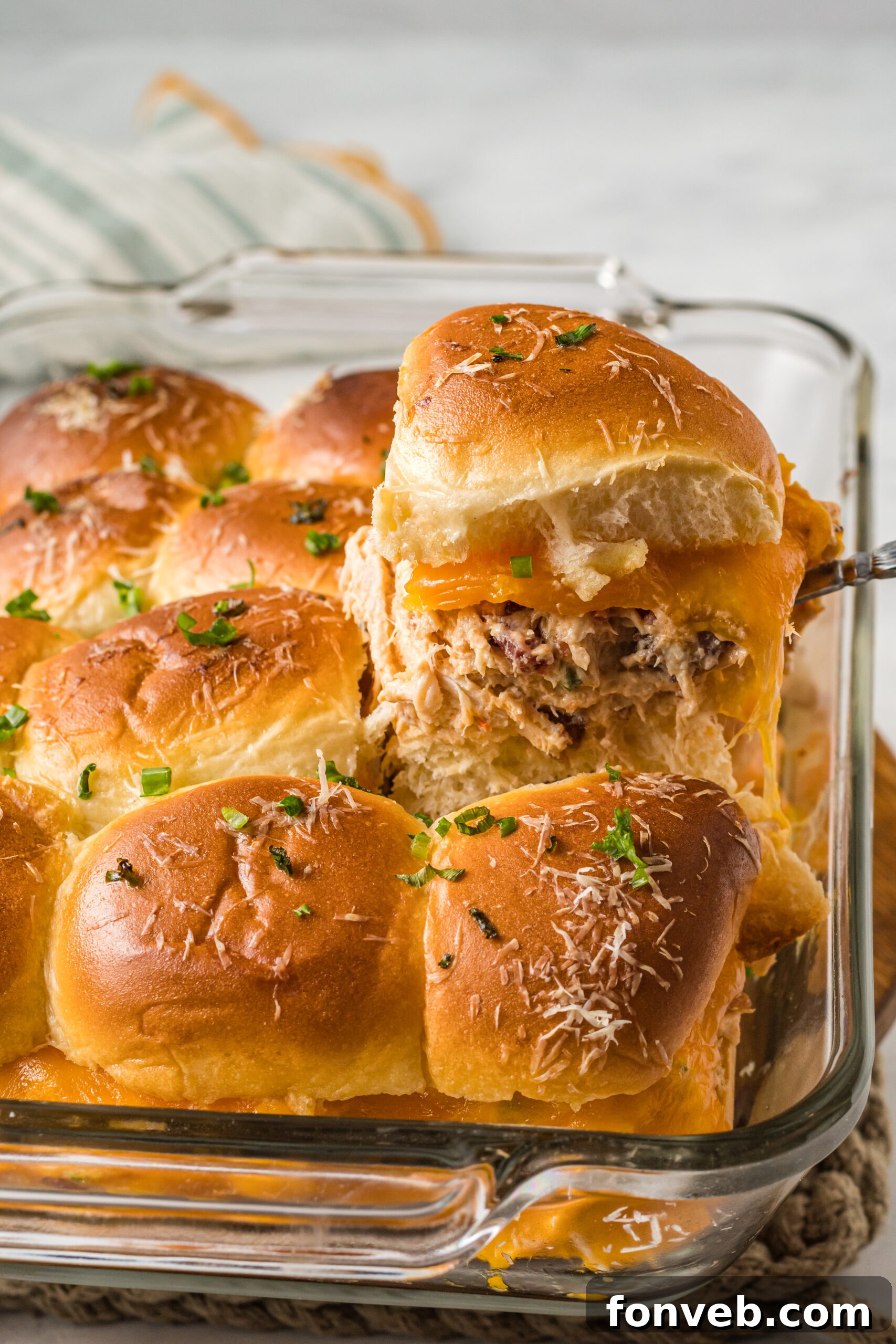 Side view of Crack Chicken Sliders in a clear baking dish with one being lifted by a silver utensil.