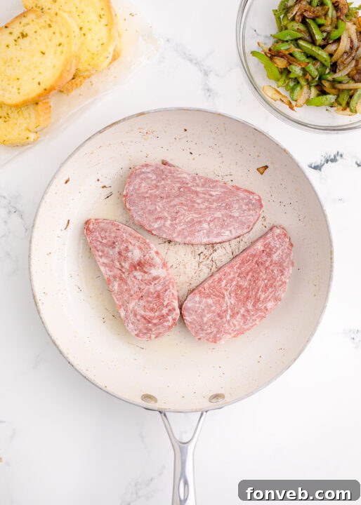 Golden Air Fryer Philly Cheesesteaks 8 Thinly sliced frozen beef steaks cooking in a pan.