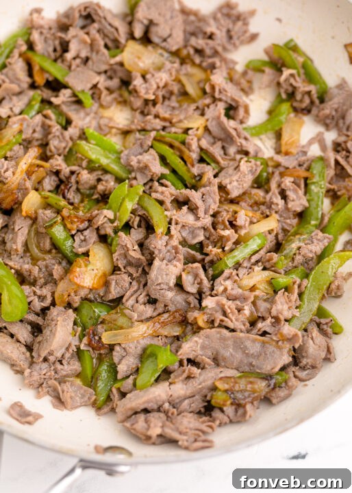 Golden Air Fryer Philly Cheesesteaks 9 Cooked beef steak being broken apart in a pan.