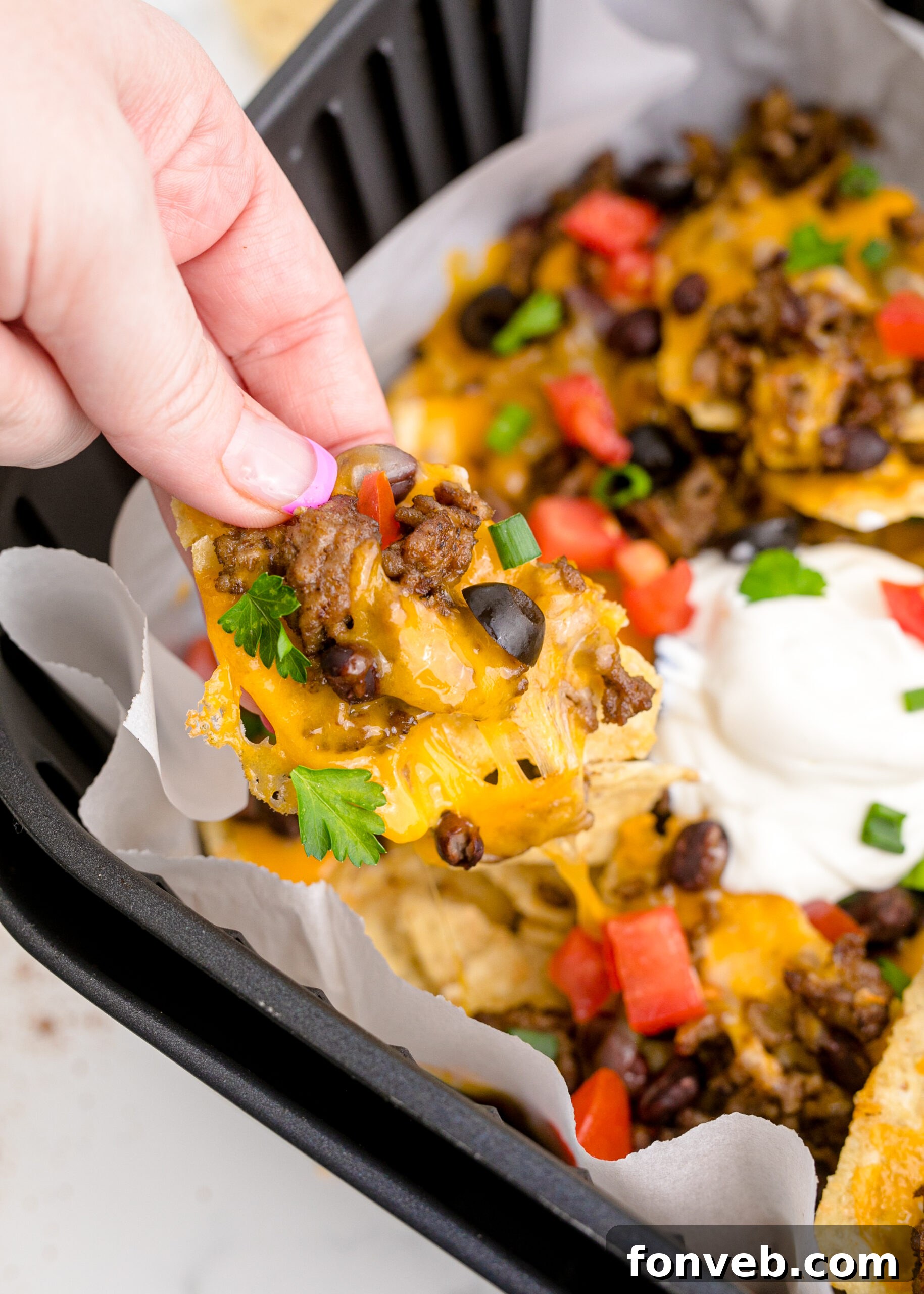 Ultimate Air Fryer Nachos 6 Up close view of Air Fryer Nachos in an air fryer basket and one nacho being held.