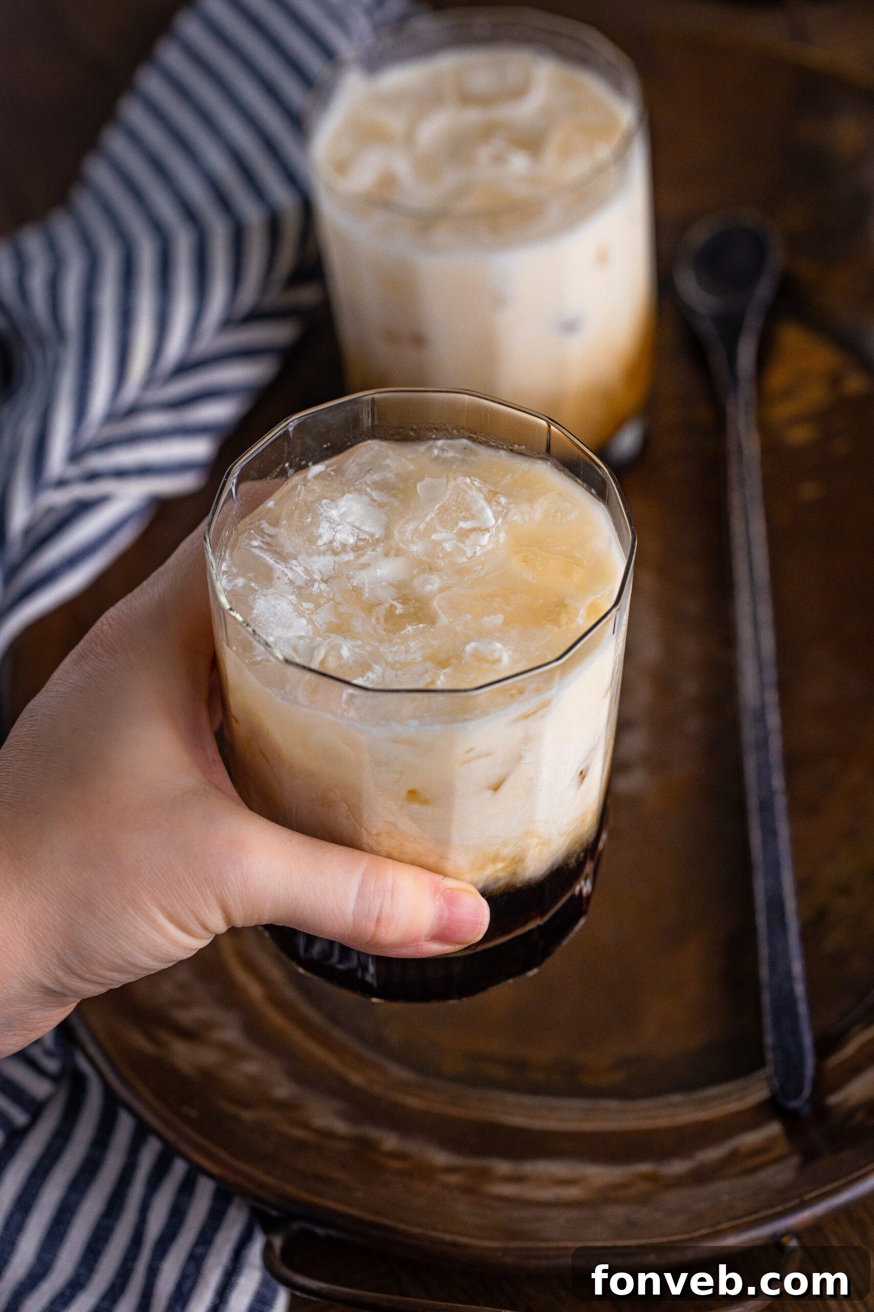 The Dude's Favorite Drink 13 A hand holding a clear glass of White Russian, showcasing the creamy texture and inviting appearance.