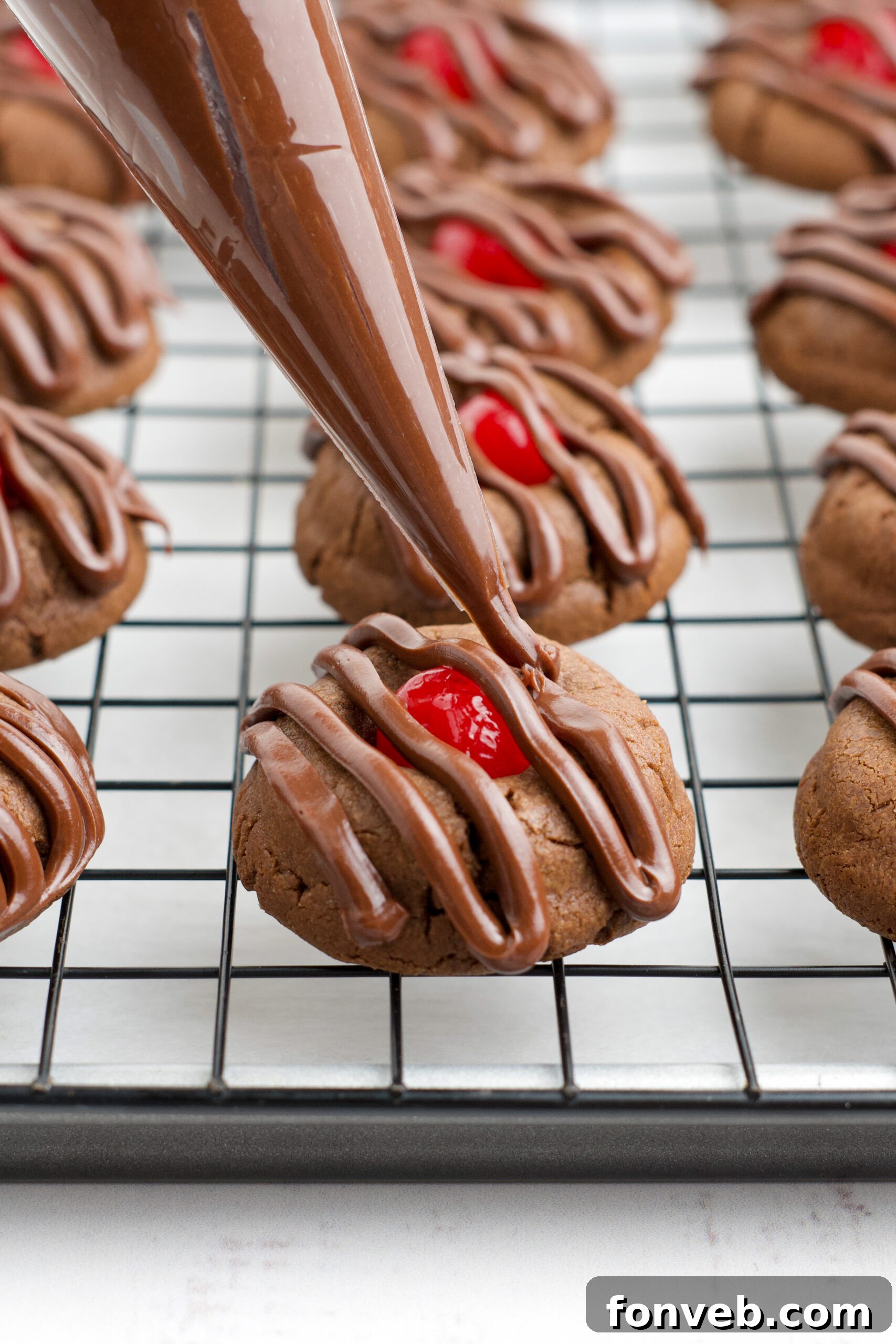 A piping bag piping on the chocolate cherry frosting onto a cookie.