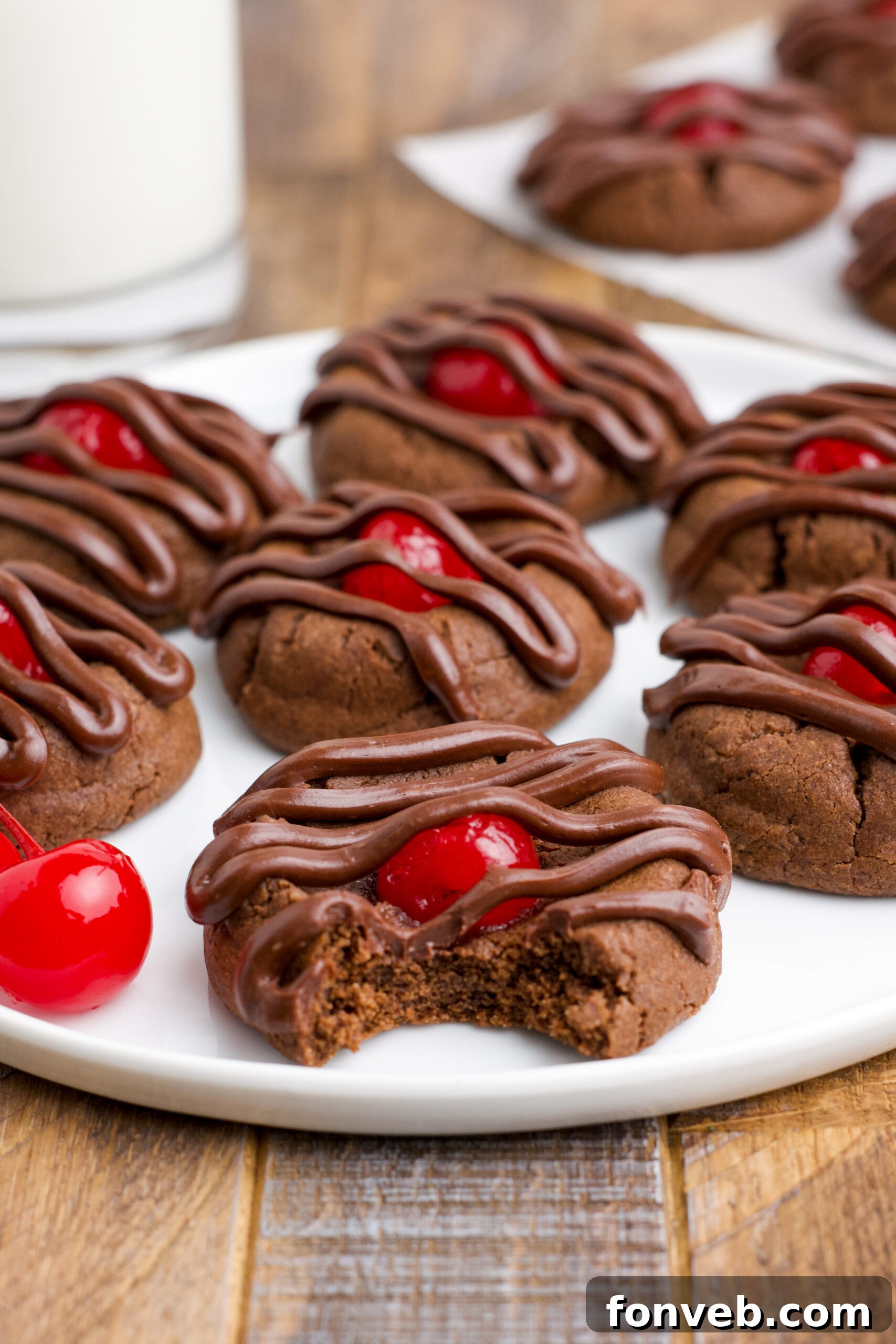 Chocolate Cherry Cookies on a white plate with a bite removed from the front cookie showing the texture inside.
