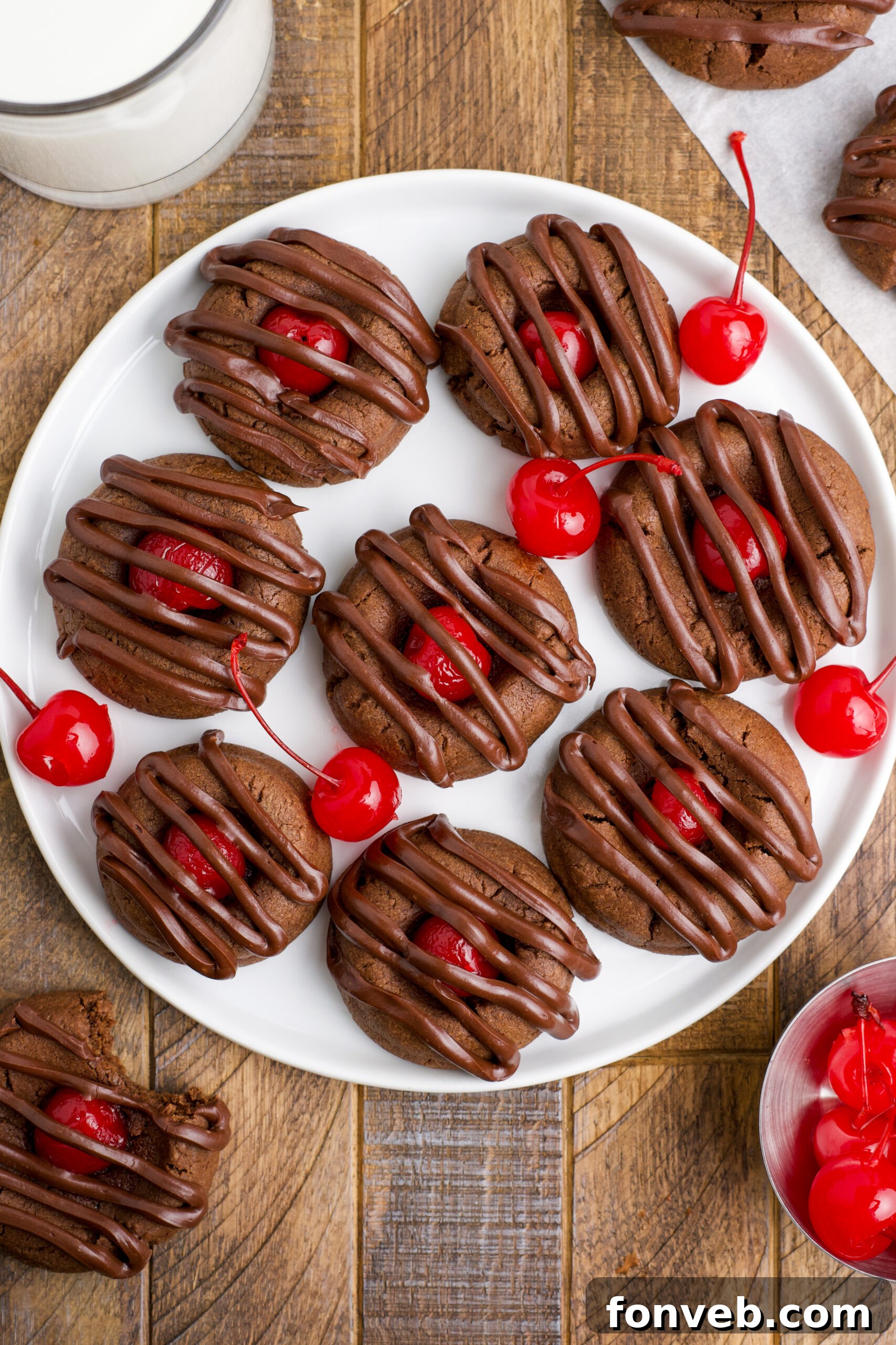 Overhead view of Chocolate Cherry Cookies on a white plate with maraschino cherries in the background.