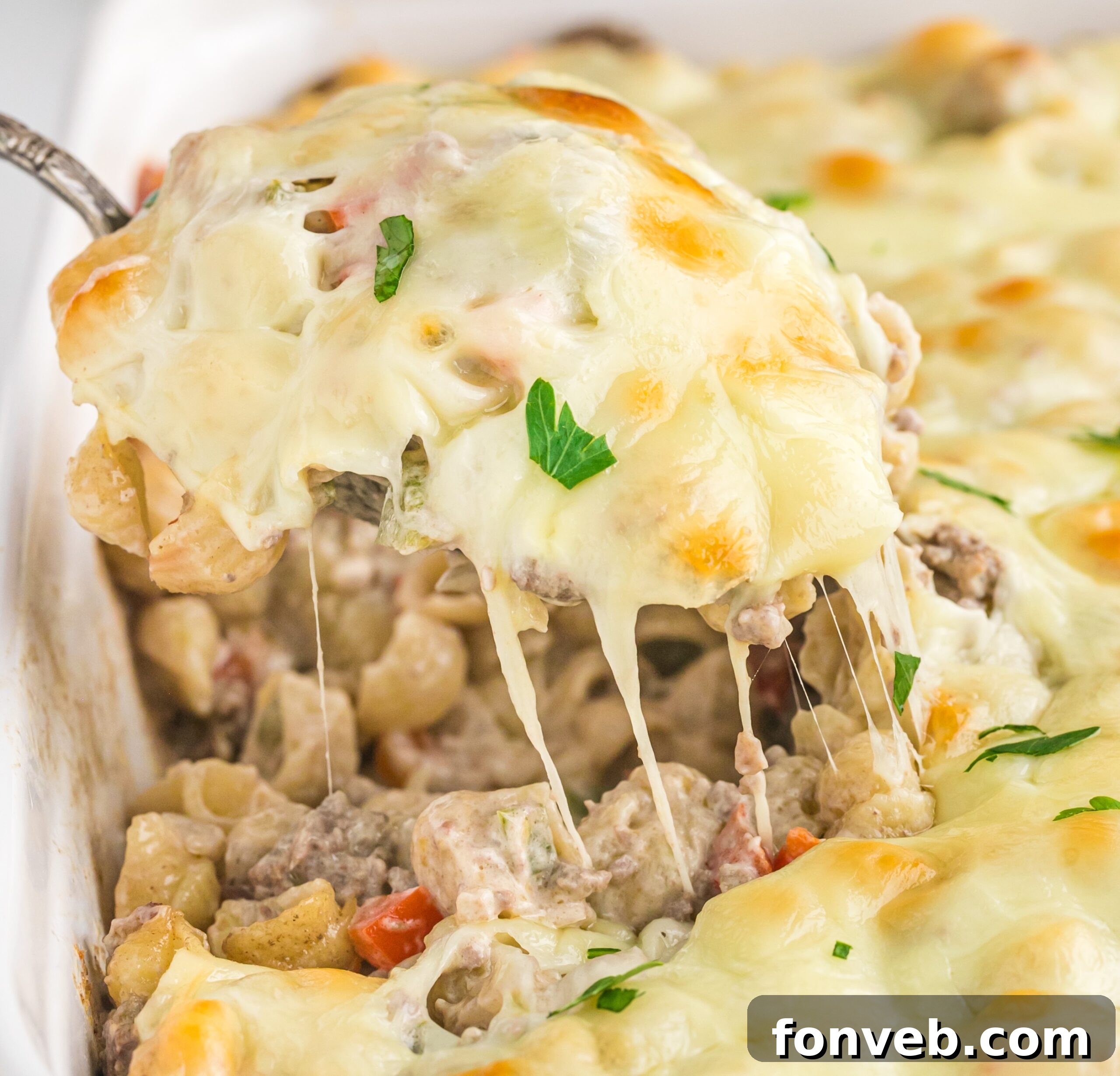 Front view of Philly Cheesesteak Casserole in a white baking dish with a silver spoon removing a spoon full.
