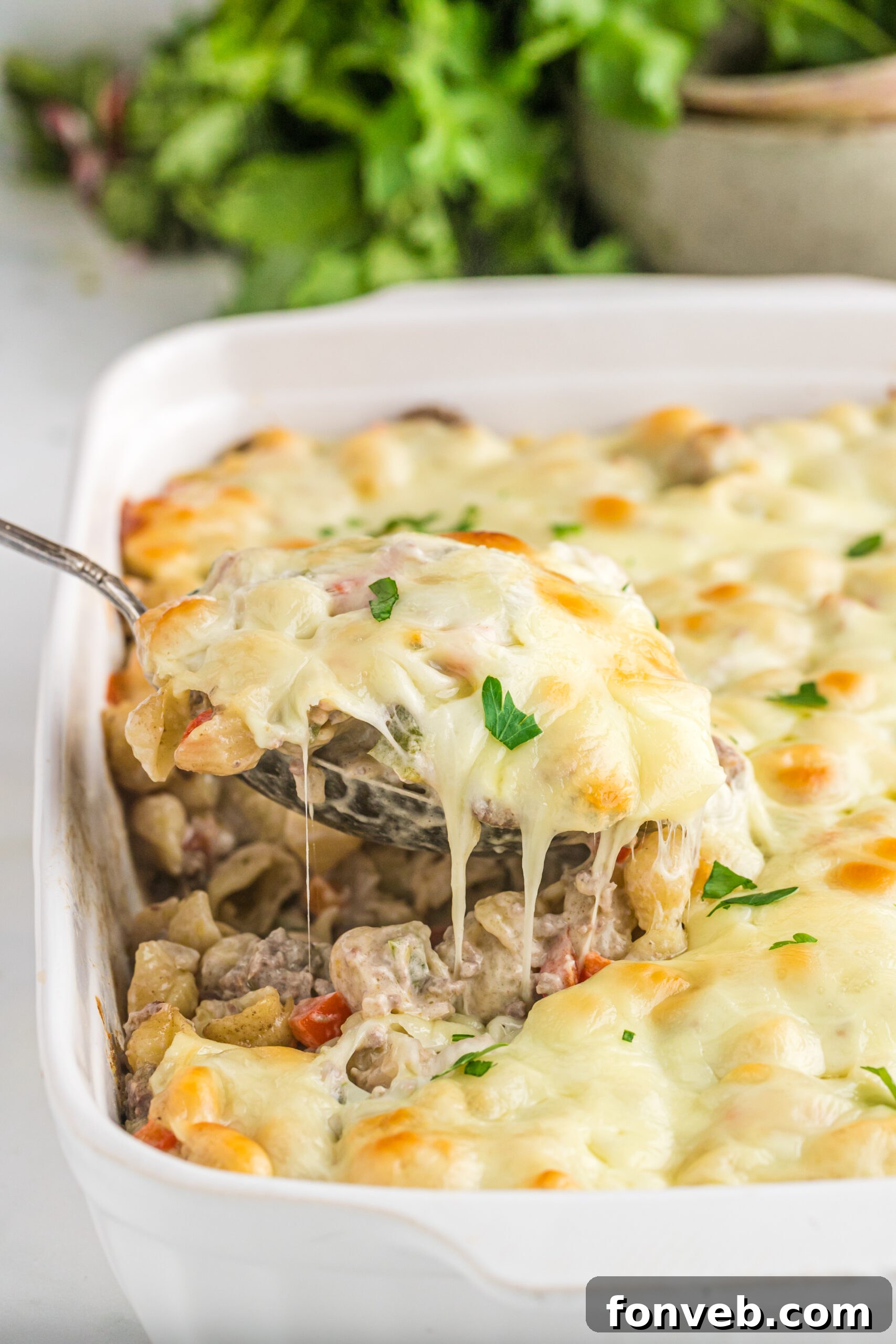 Front view of Philly Cheesesteak Casserole in a white baking dish with a silver spoon removing a spoon full.