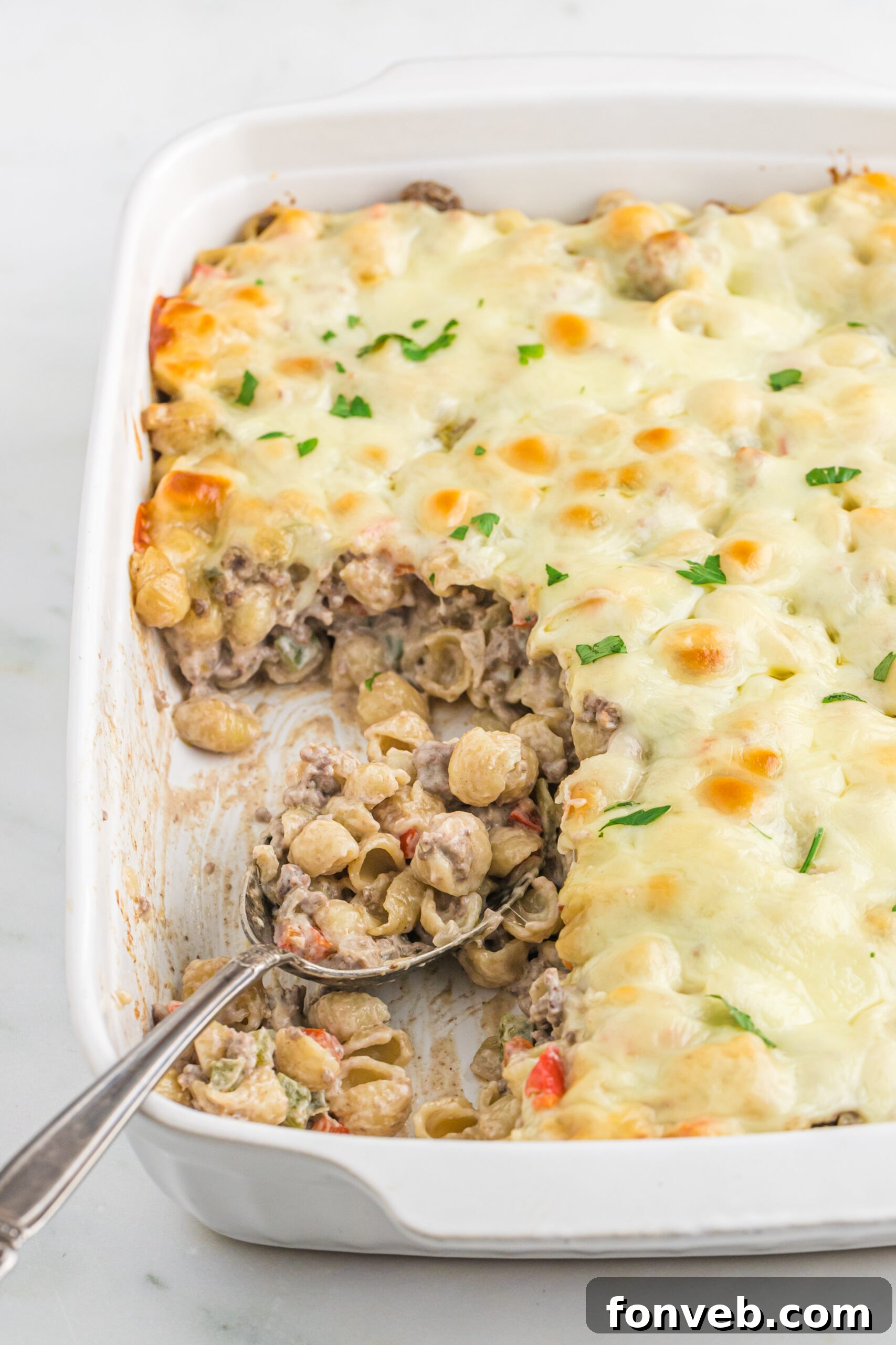 Front view of Philly Cheesesteak Casserole in a white baking dish with a silver spoon.