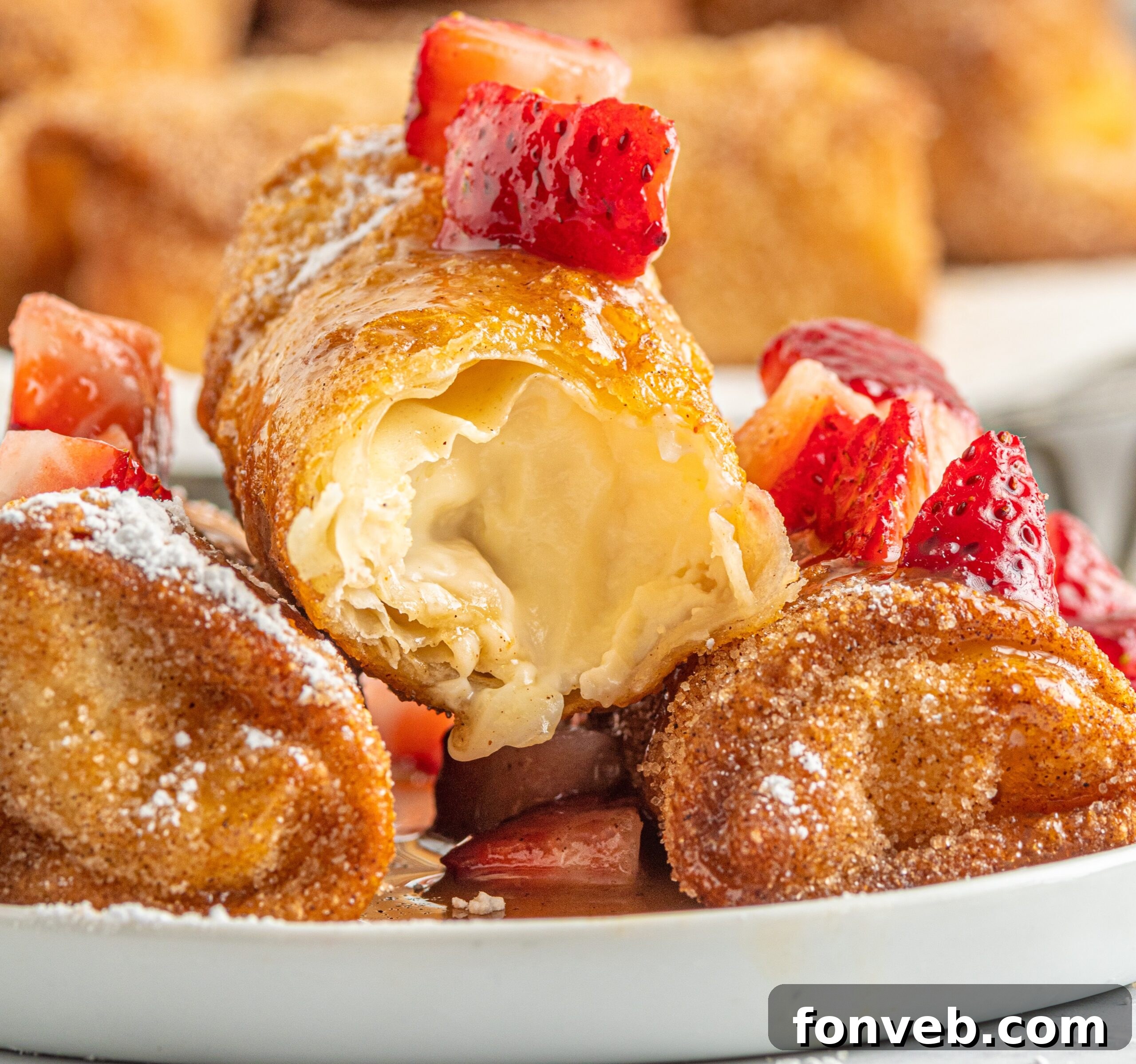 Golden-brown Cheesecake Eggrolls on a white plate, some cut open to reveal the creamy filling, garnished with fresh sliced strawberries and a drizzle of sauce.