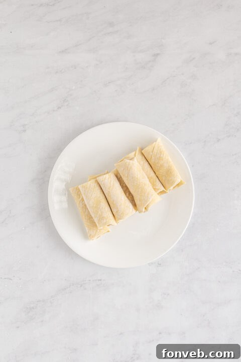 Step-by-step image of rolling the egg roll wrapper tightly to seal.