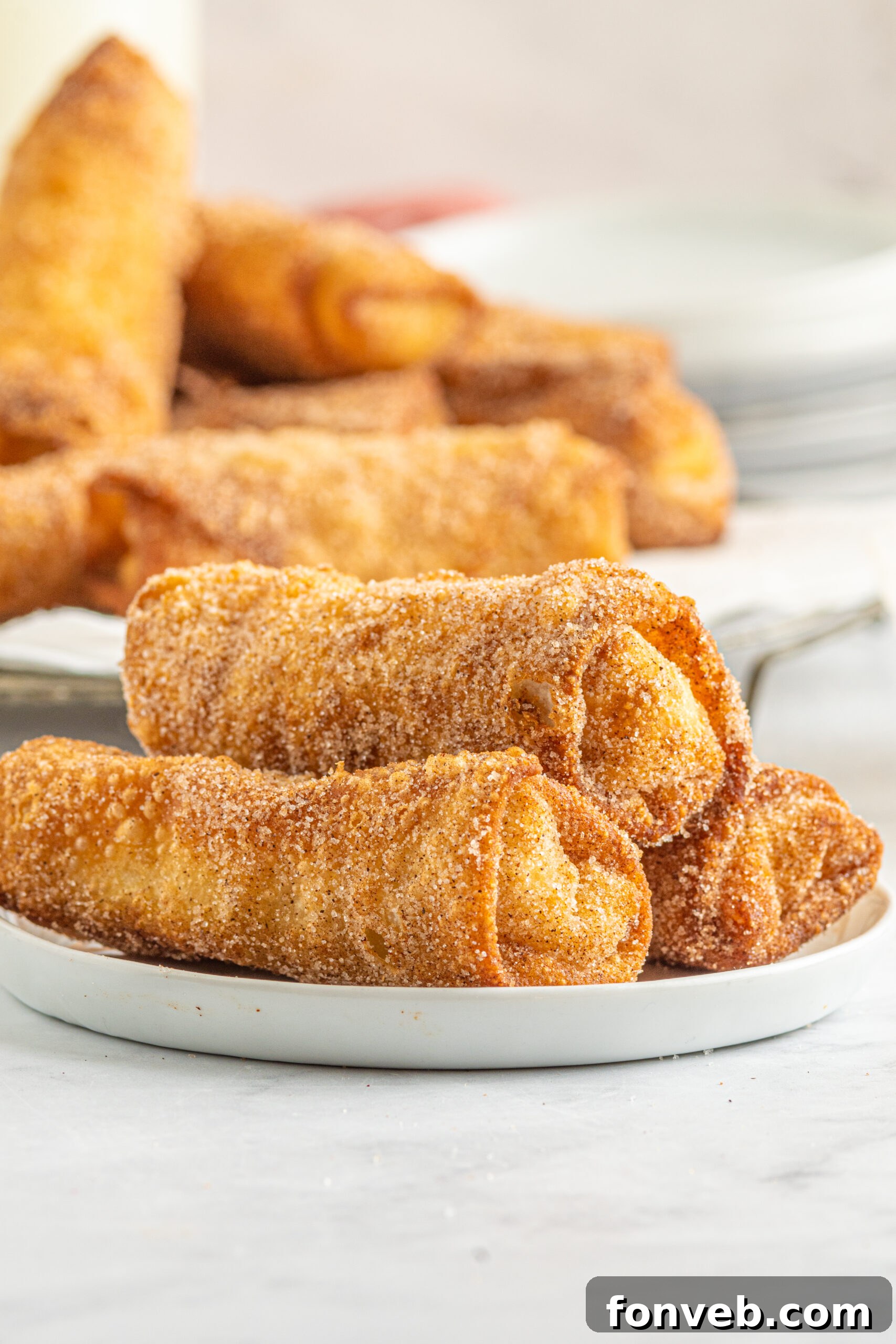 Front view of three perfectly golden and crispy Cheesecake Egg Rolls stacked on a clean white plate, ready to be enjoyed.