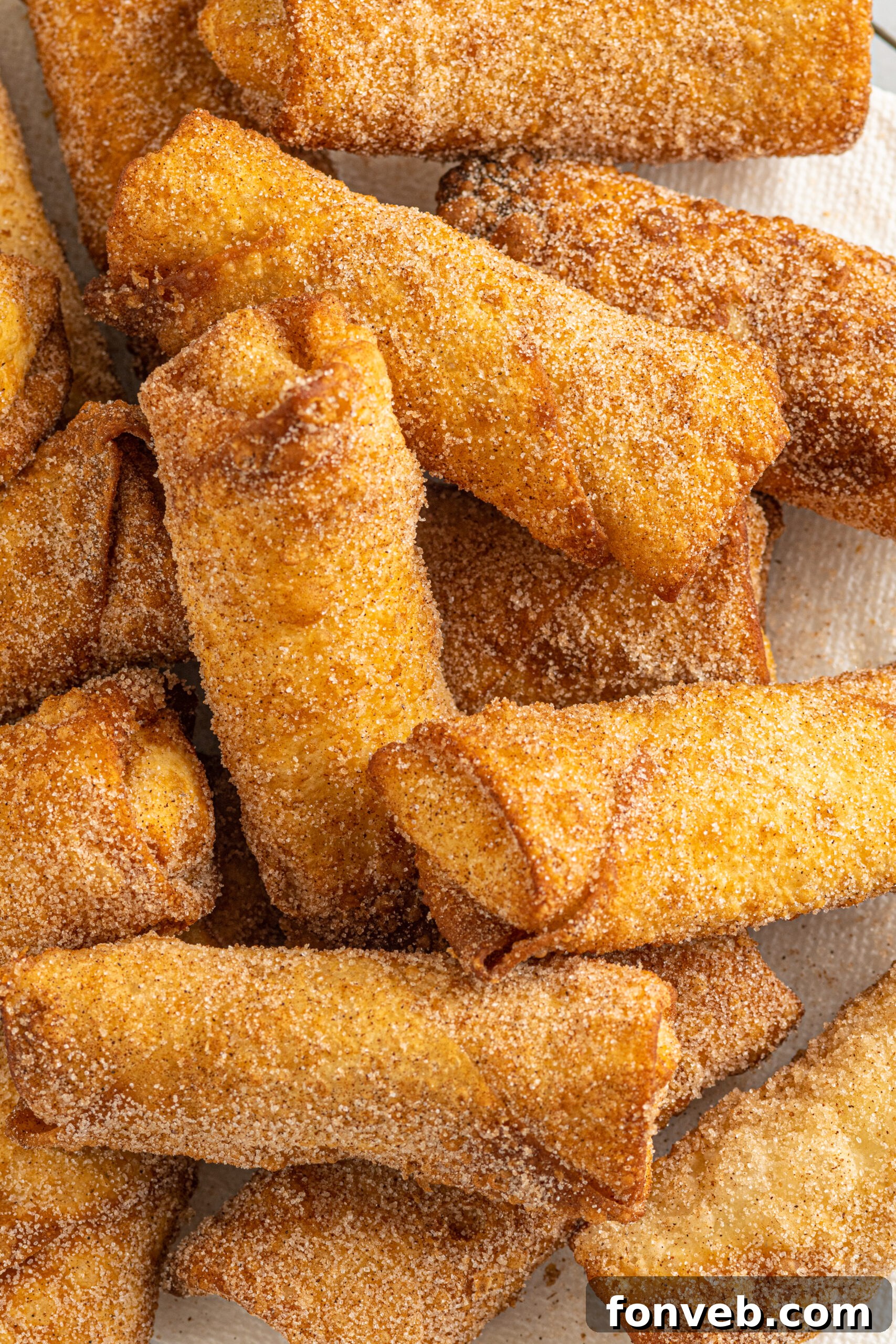 Overhead view of several beautifully fried Cheesecake Egg Rolls arranged on a white serving platter, showcasing their enticing golden color.