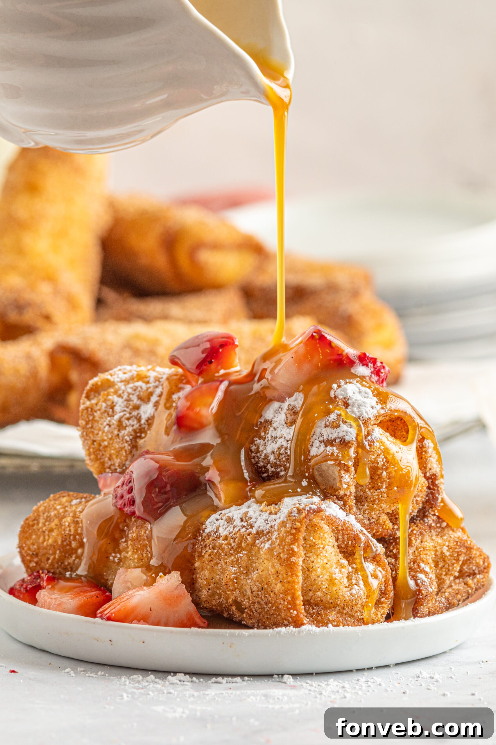 A plate of Cheesecake Egg Rolls generously dusted with powdered sugar, topped with fresh strawberries, and drizzled with sweet caramel sauce for an elegant presentation.