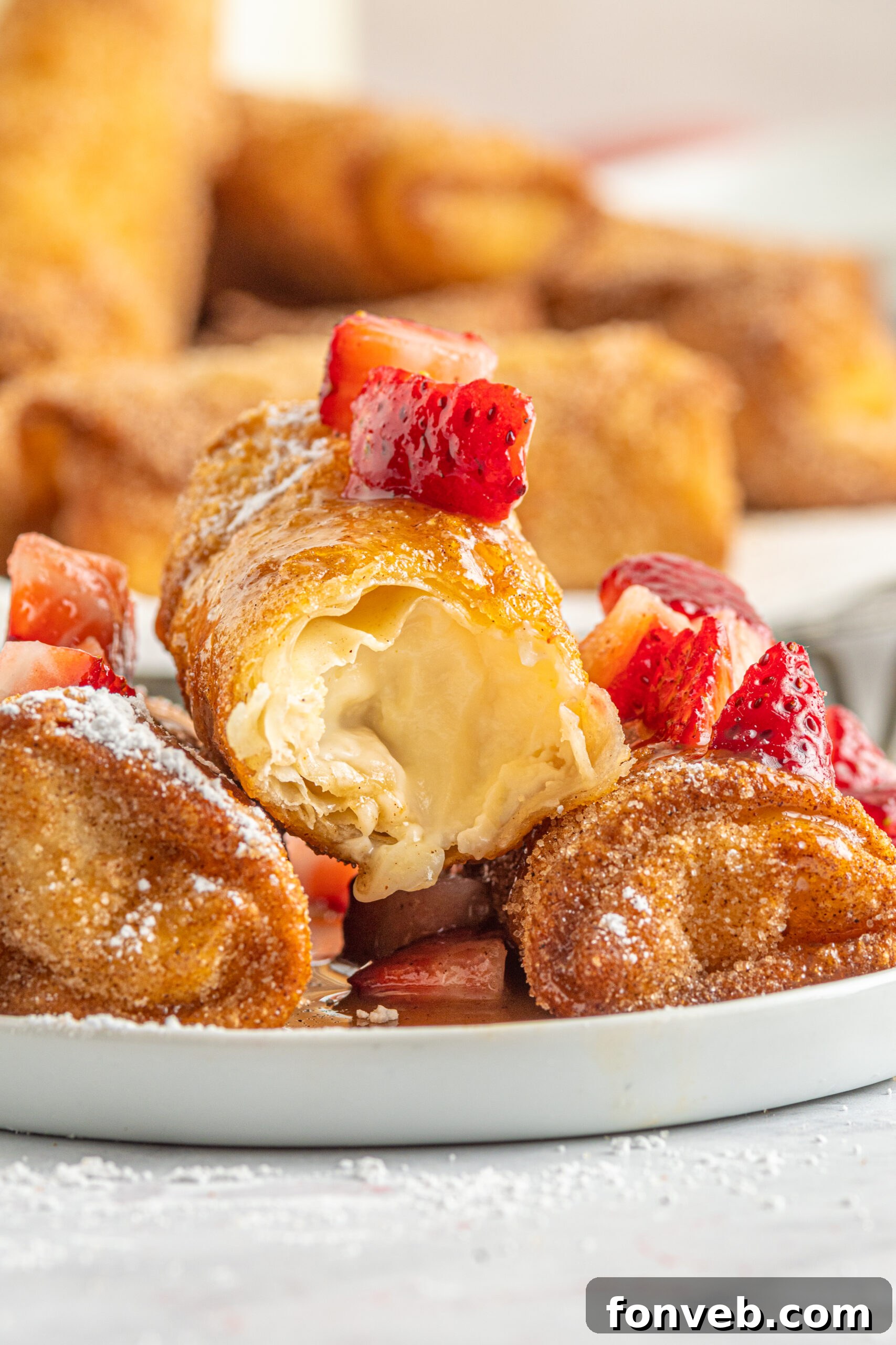 Close-up front view of Cheesecake Egg Rolls, one with a bite taken, showcasing the creamy interior, artfully arranged on a plate with powdered sugar, fresh strawberries, and caramel.