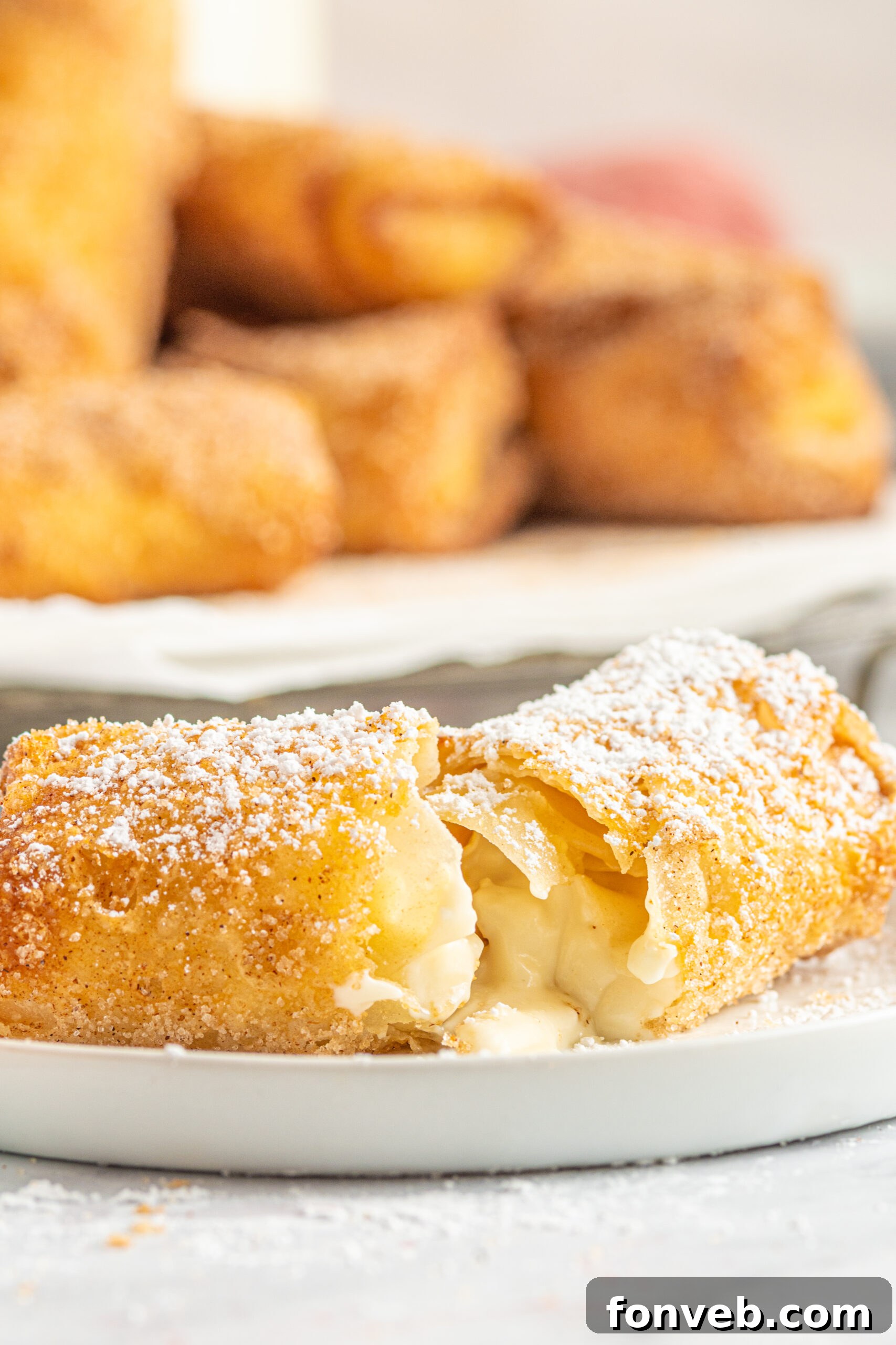 Side view of a perfectly fried Cheesecake Egg Roll, expertly split in half to reveal its creamy, tempting interior, resting on a white plate.