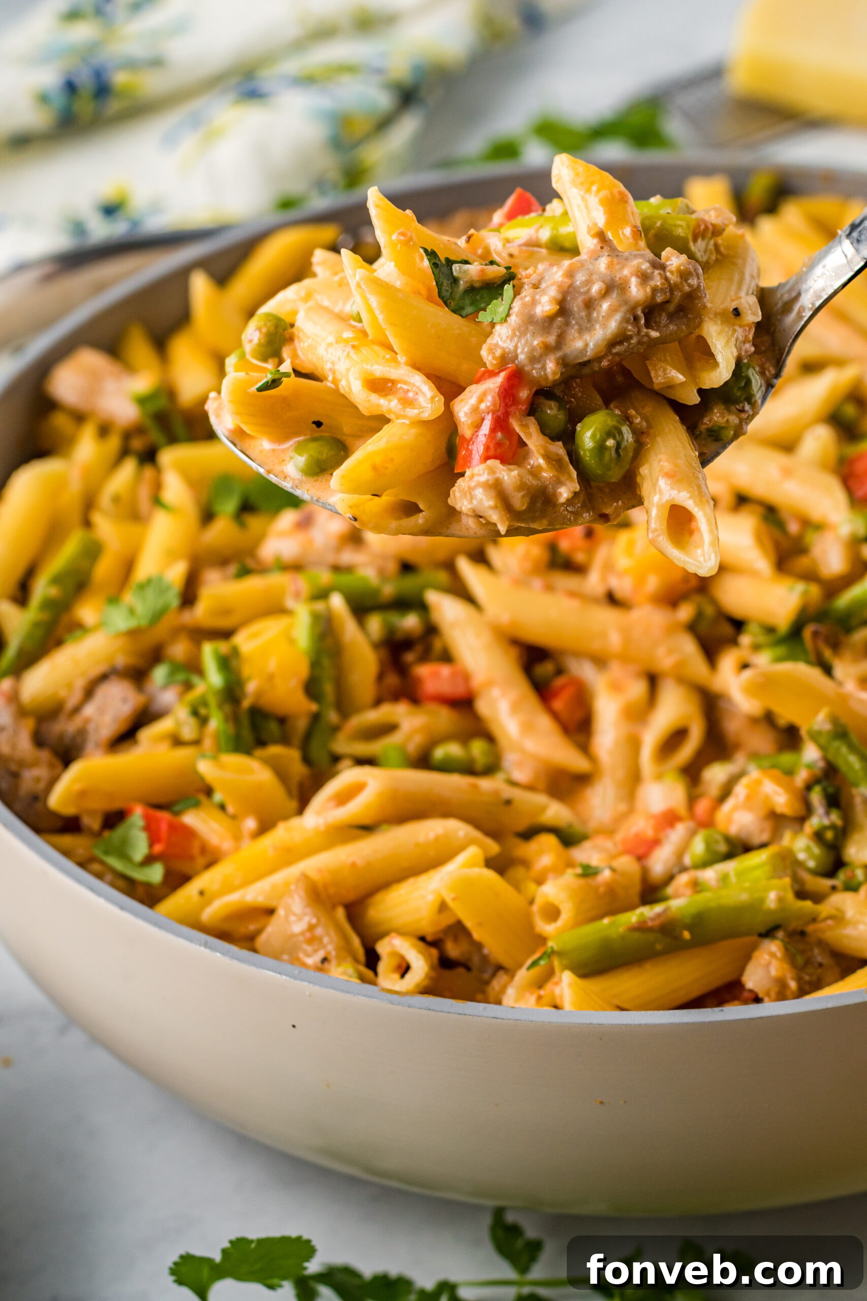 A close-up of a large spoon scooping a generous portion of Cajun Chicken Pasta, showing the creamy sauce coating the pasta and chicken.