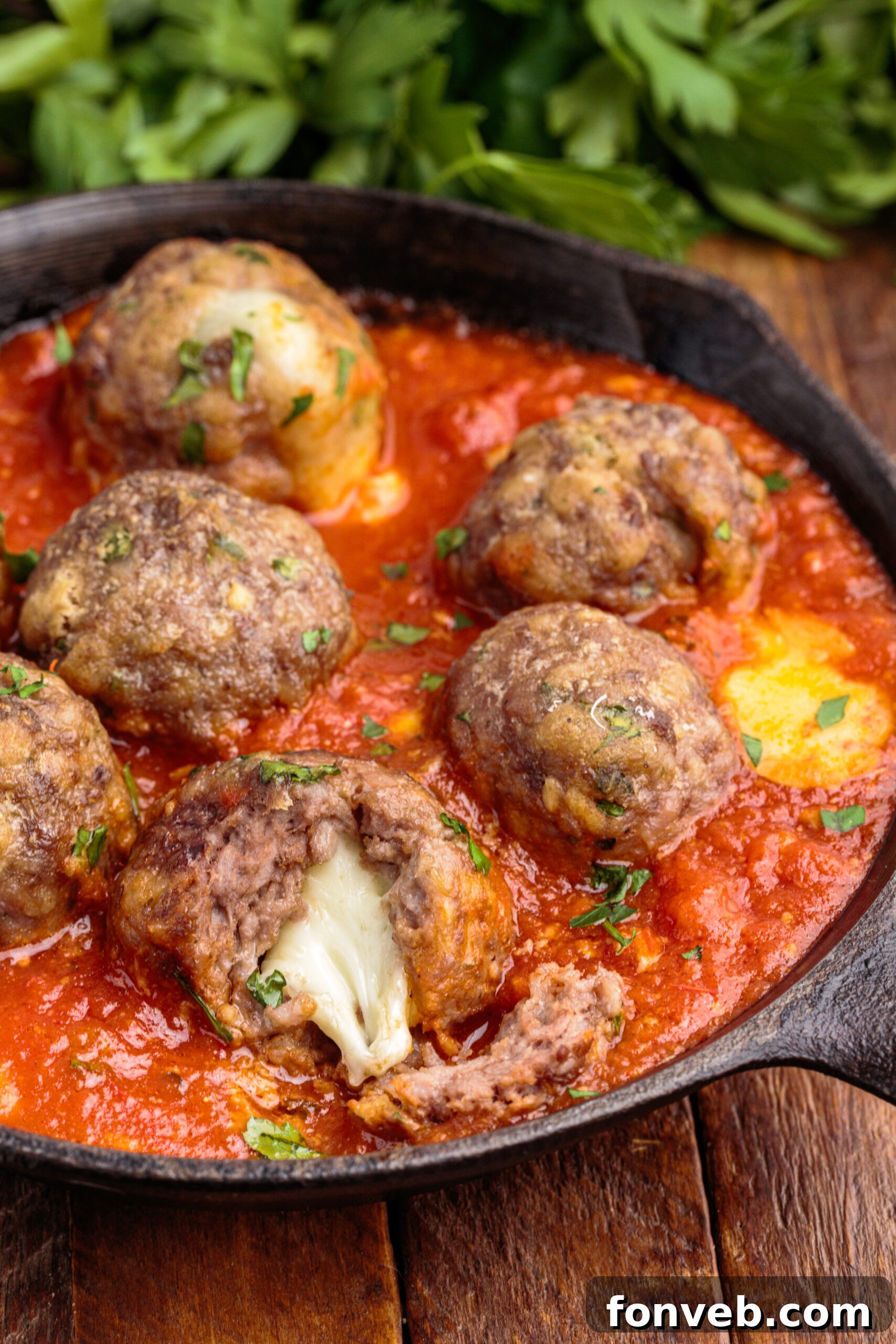 Overhead view of Mozzarella Stuffed Meatballs in a cast iron skillet with one meatball cut open by a silver fork, revealing melted mozzarella.