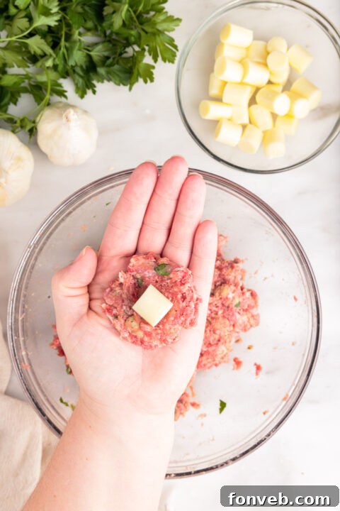 Hands gently shaping the meatball mixture around the mozzarella cube.