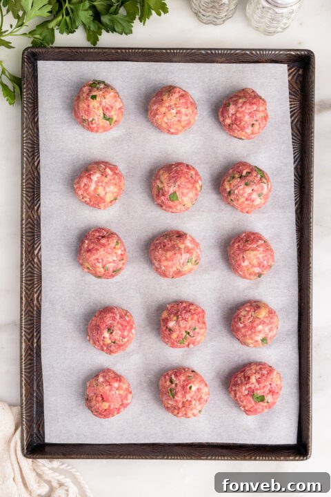 Several raw mozzarella stuffed meatballs neatly arranged on a parchment-lined baking sheet.