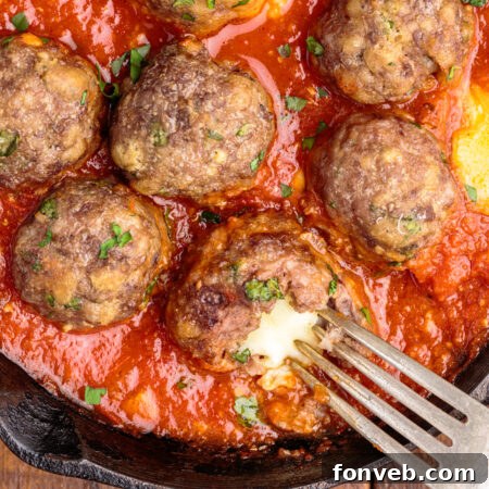 Overhead view of Mozzarella Stuffed Meatballs in a cast iron skillet with one meatball cut open by a silver fork.