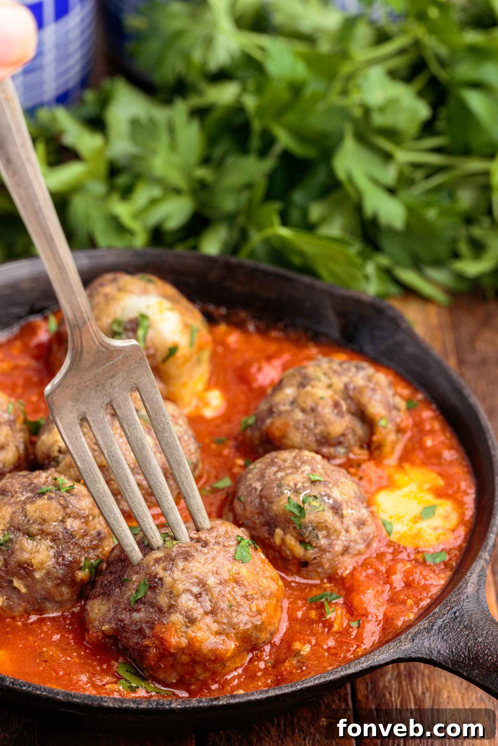 Side view of Mozzarella Stuffed Meatballs in a cast iron skillet with a silver fork impaling a meatball, showcasing the melted cheese.