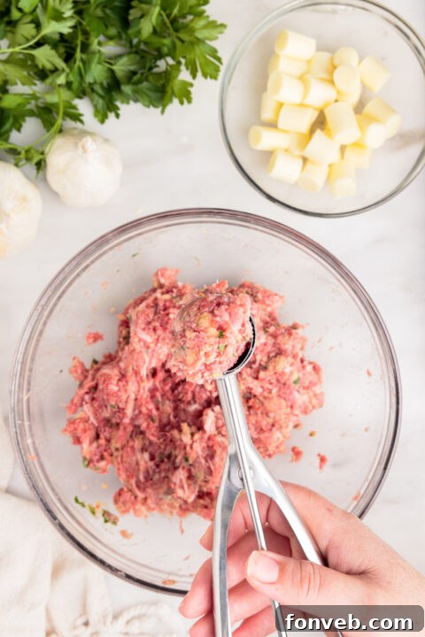 A small cube of mozzarella cheese being placed into the center of a meatball portion.