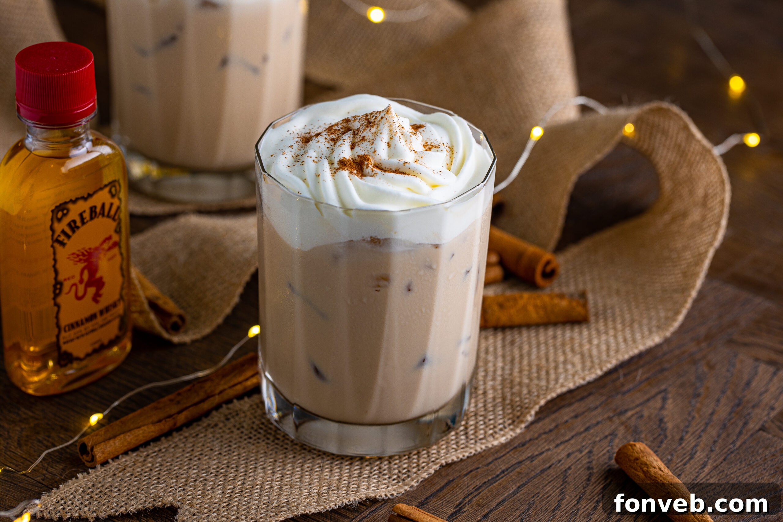 The cinnamon roll cocktail in a clear glass topped with whipped cream and dusted with cinnamon. 