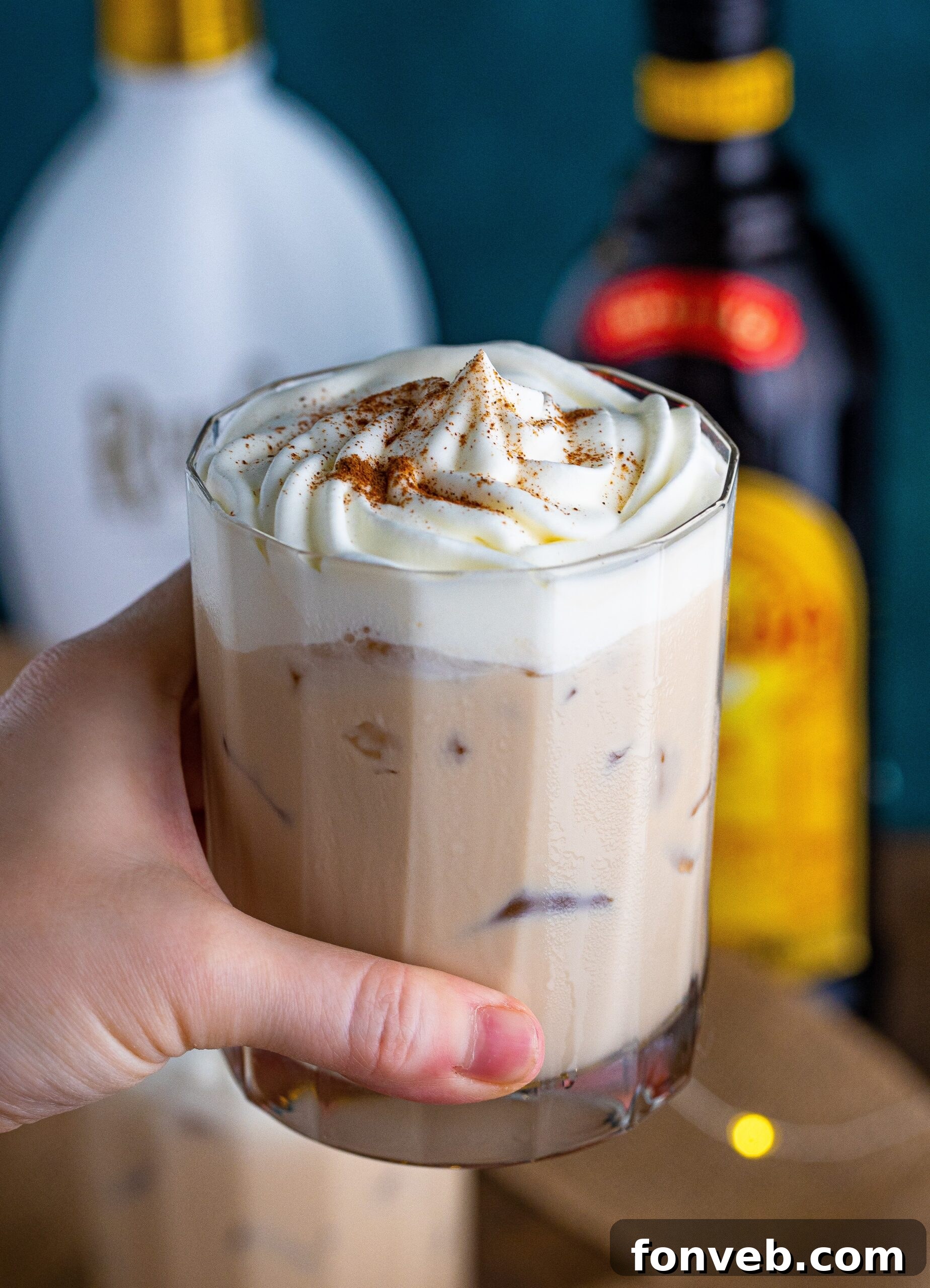 a hand holding up a glass of cinnamon roll cocktail