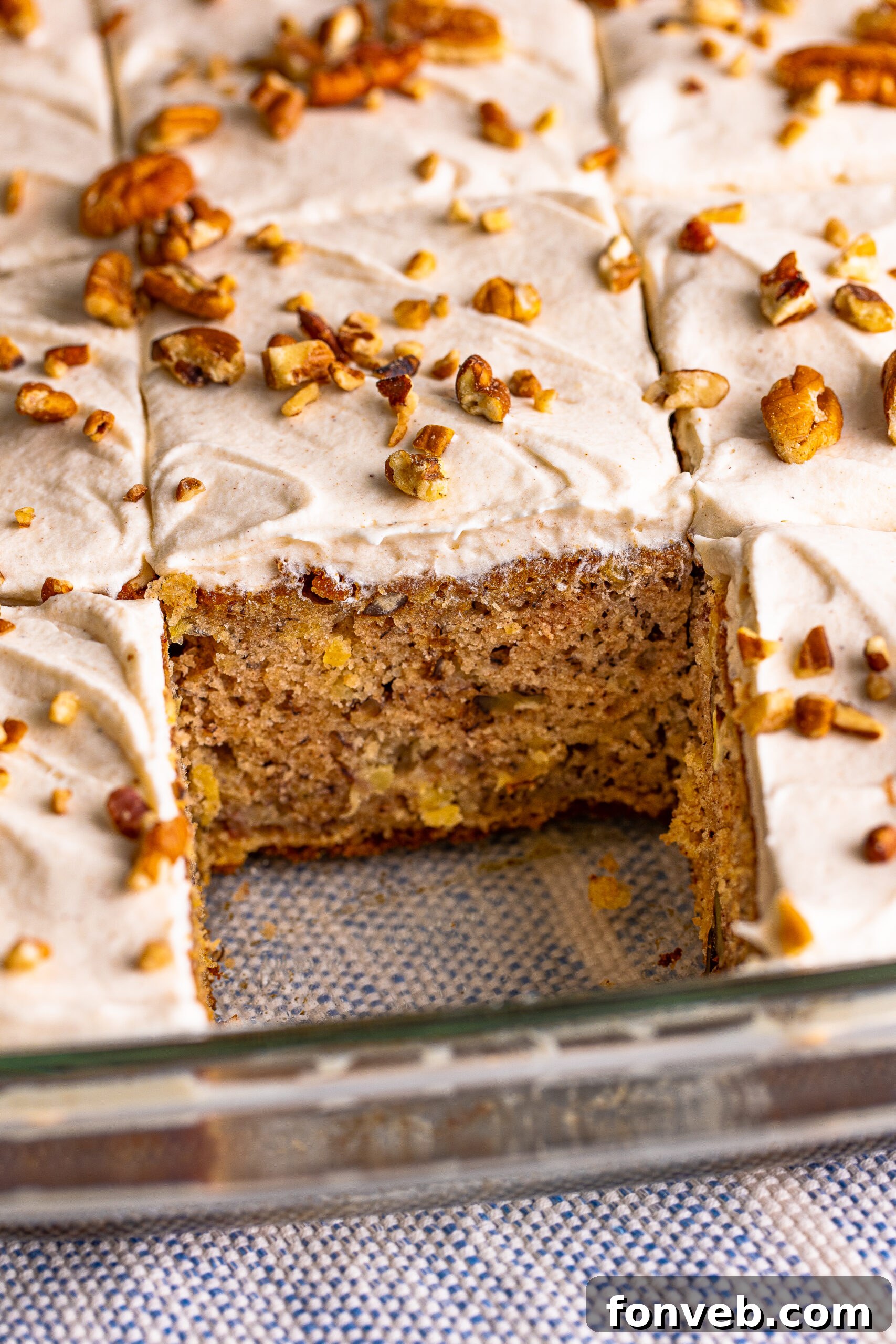 A slice of Hummingbird Cake has been cut from a larger baking dish, revealing its rich, moist interior and delicious frosting.