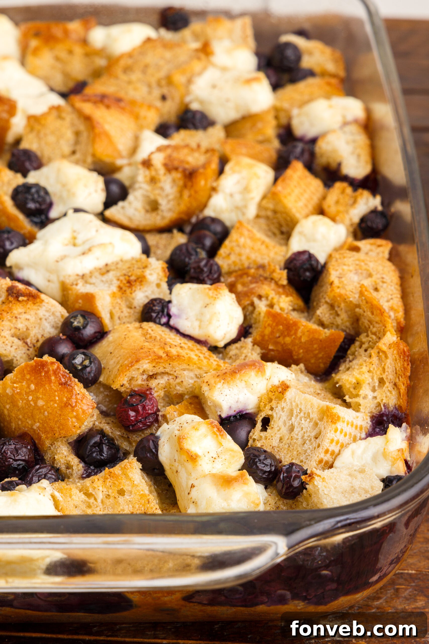 A close-up view of the Blueberry French Toast Casserole in a clear glass baking dish, showing the golden-brown crust, plump blueberries, and creamy texture.