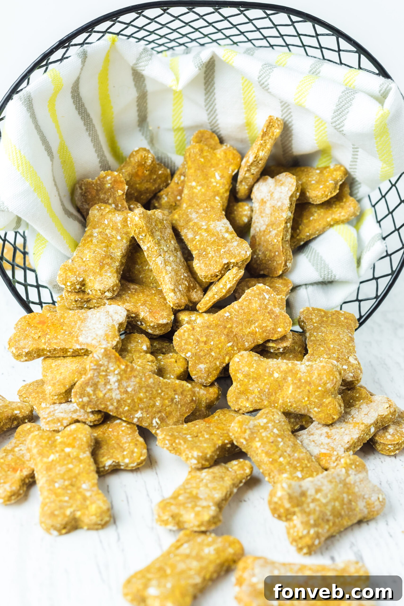 Front view of an overflowing wire basket filled with homemade Sweet Potato and Pumpkin Dog Treats, with several treats artfully spilling out, emphasizing their abundance and homemade charm.
