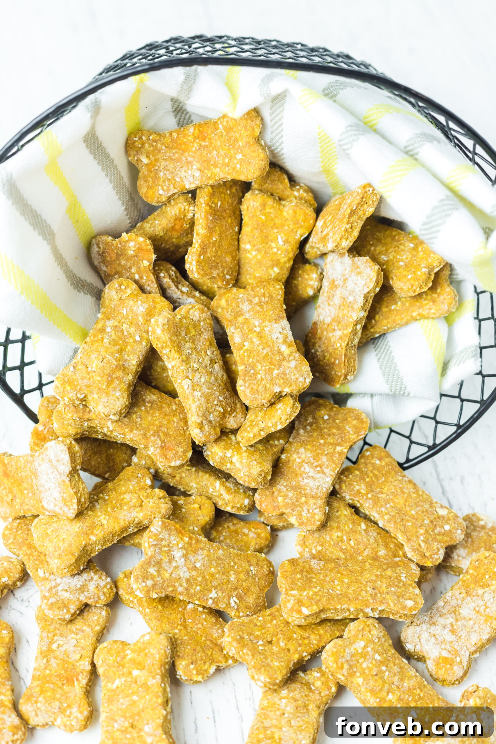 A generous quantity of Sweet Potato and Pumpkin Dog Treats spilling from a wire basket onto a linen surface, inviting viewers to imagine their dog enjoying these healthy snacks.