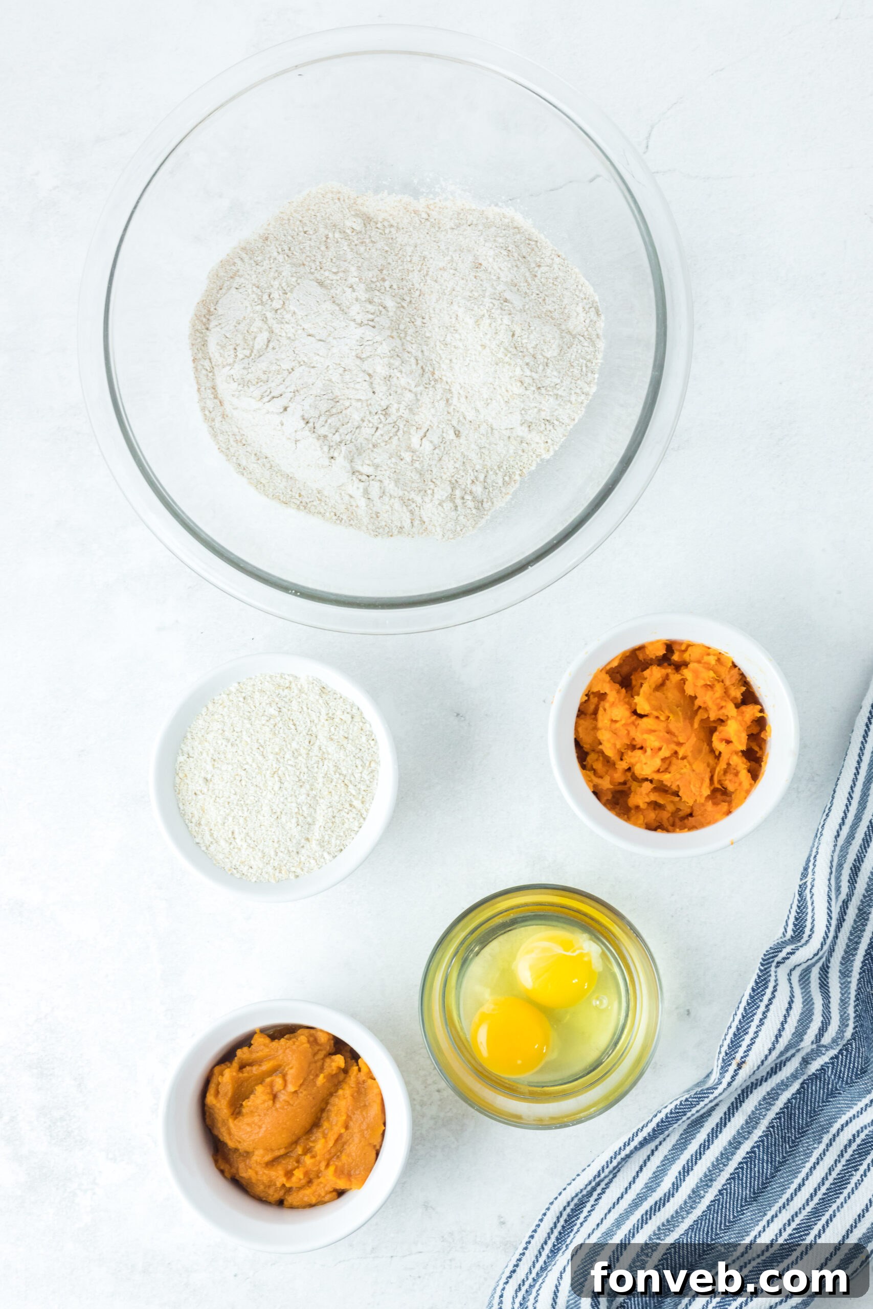 Overhead shot displaying all the essential ingredients for the Sweet Potato and Pumpkin Dog Treats recipe laid out neatly, including whole wheat flour, rolled oats, canned pumpkin, mashed sweet potato, and eggs.