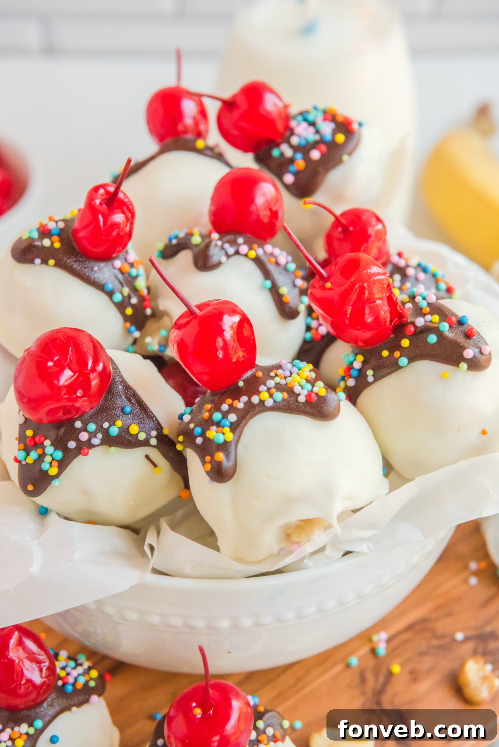Front view of golden-brown Banana Split Truffles nestled in a pristine white bowl, showcasing their smooth chocolate coating and perfect spherical shape.