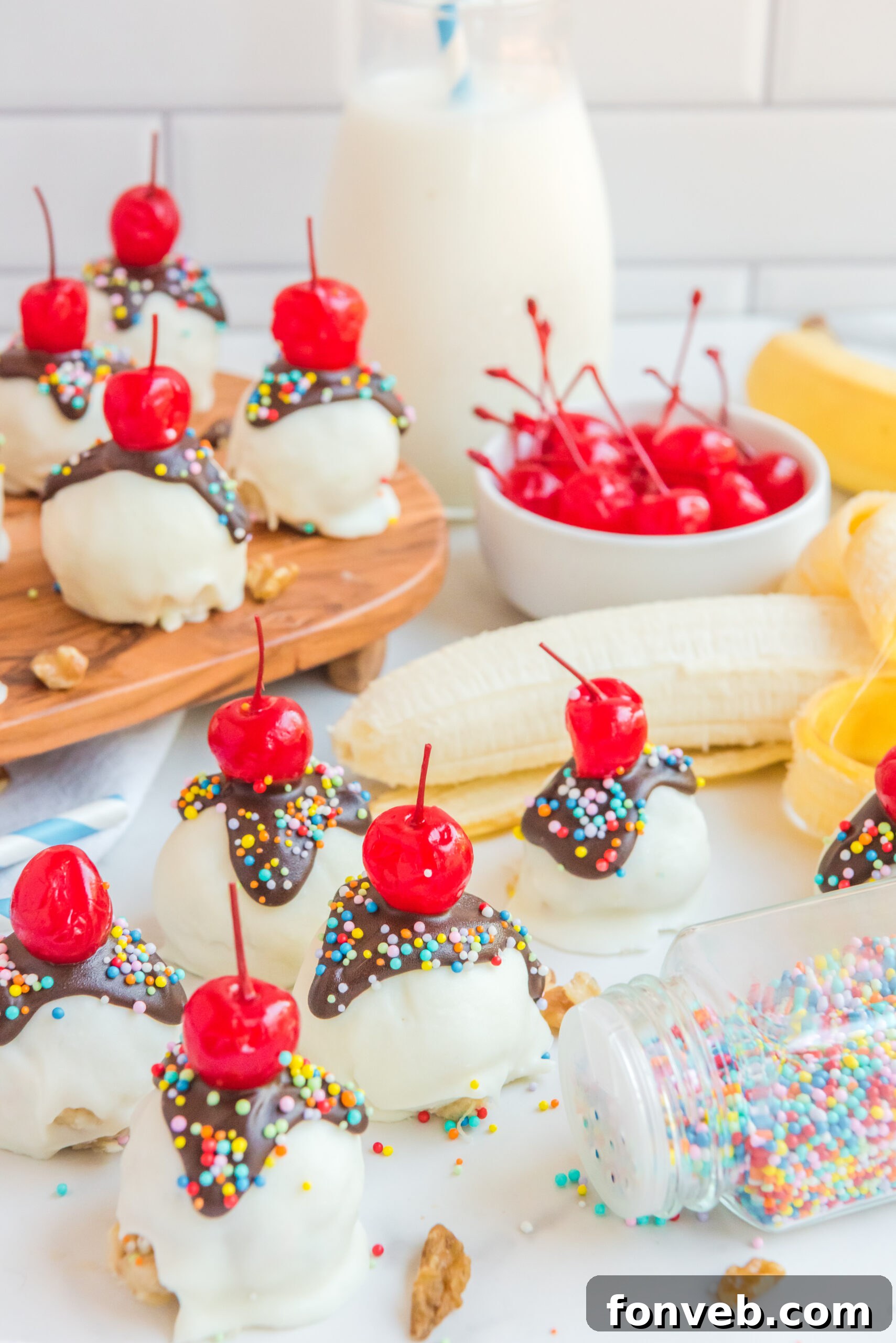 A visually appealing arrangement of Banana Split Truffles, complemented by fresh banana slices, a bowl brimming with maraschino cherries, and scattered nuts, creating a vibrant still life.