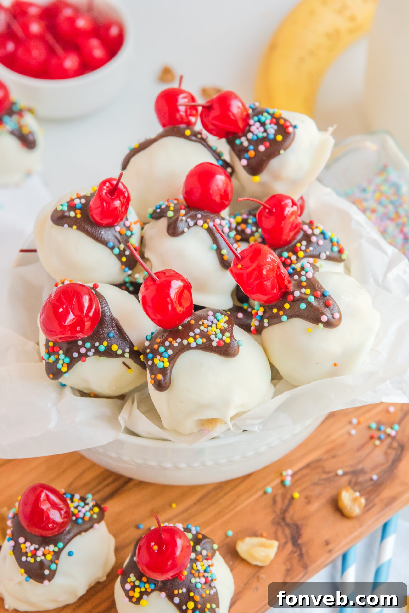 An overhead shot of an assortment of Banana Split Truffles artfully arranged, surrounded by fresh cherries, chopped nuts, and sliced bananas, illustrating the classic dessert inspiration.