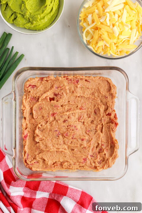 Step 3: Carefully spreading a layer of sour cream over the guacamole, maintaining distinct layers.