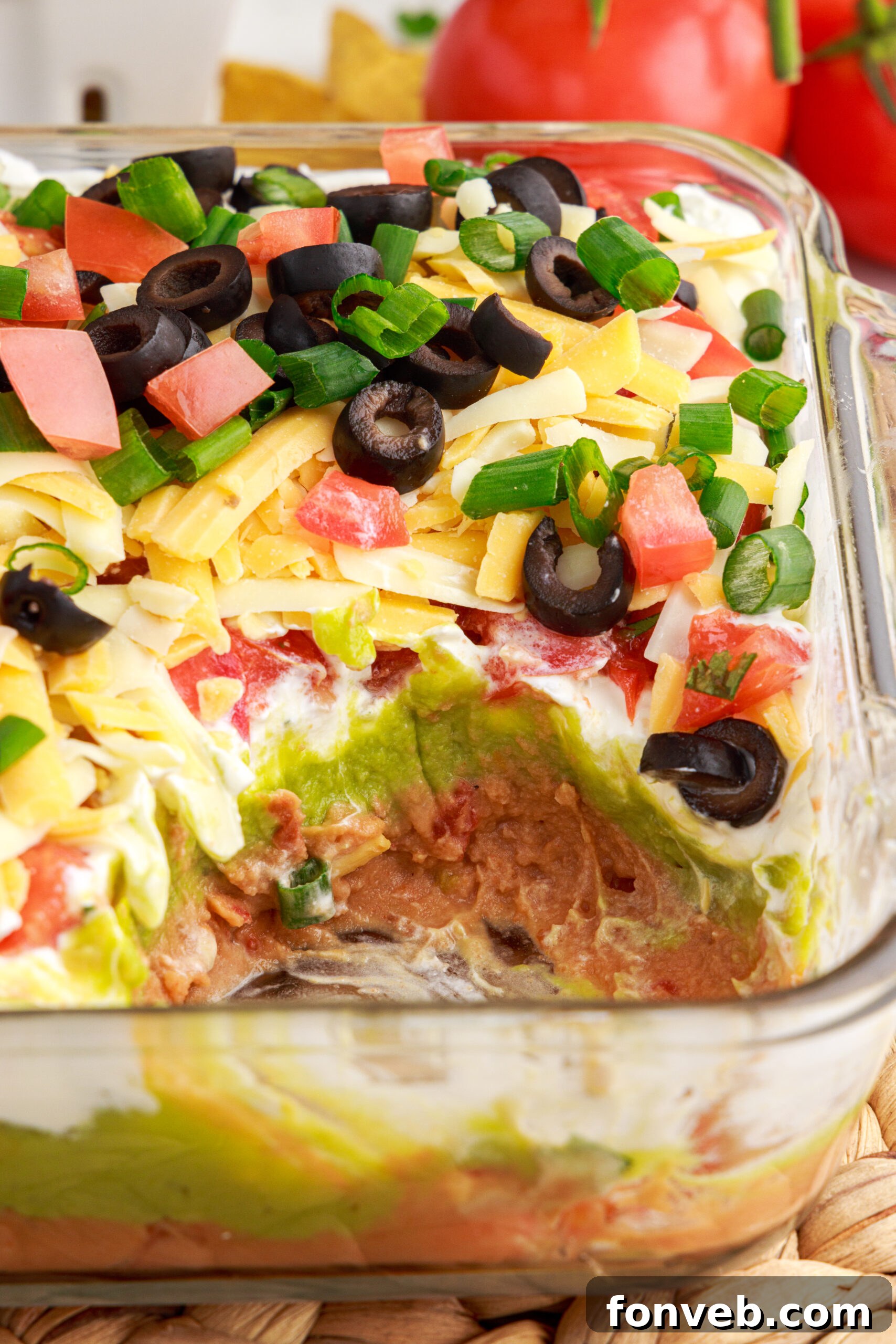 A close-up view of the 7-Layer Dip in a clear baking dish, with a portion already scooped out, emphasizing its readiness for enjoyment.