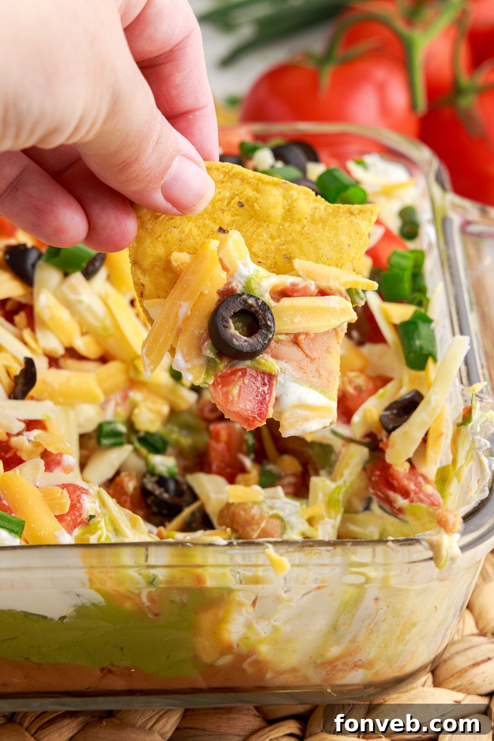 A close-up image showing a single tortilla chip generously dipped into the vibrant and creamy 7-Layer Dip.