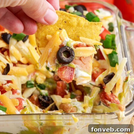 A close-up image of a tortilla chip dipped into the delicious 7-Layer Dip, highlighting its rich textures and colors.