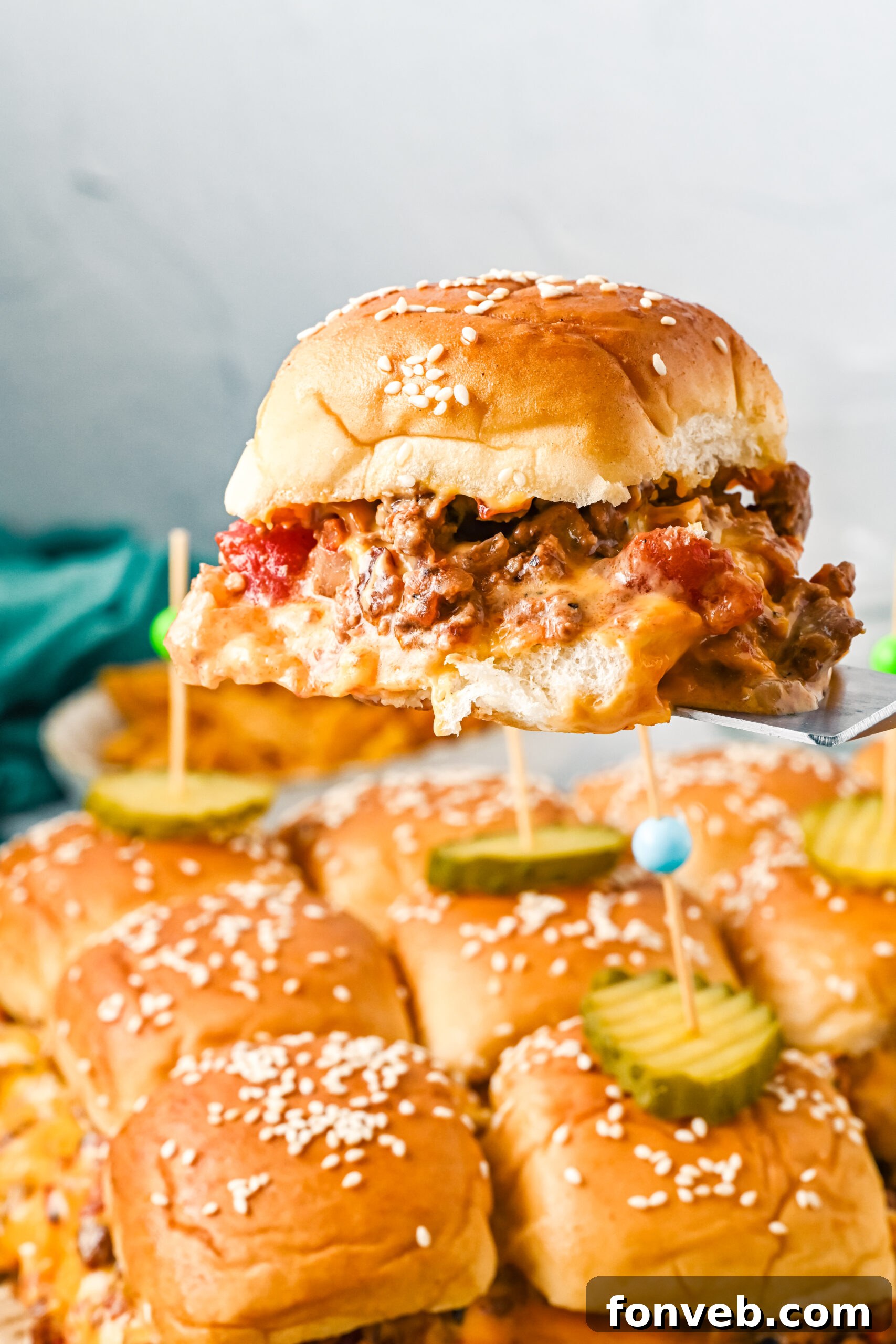 A perfectly cooked cheeseburger slider, topped with bacon and cheese, resting on a silver spatula, ready to be served.