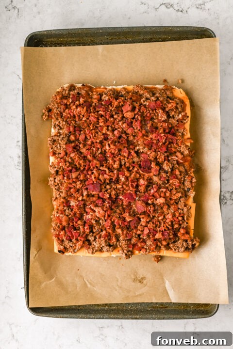Slider buns sliced in half horizontally, with mayonnaise spread on the bottom halves in a baking pan.